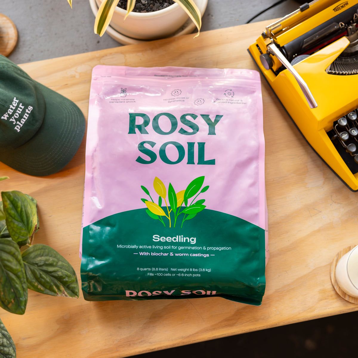 Bag of Rosy Soil Seedling mix, designed for germination and propagation, placed on a wooden table with plants and a typewriter.
