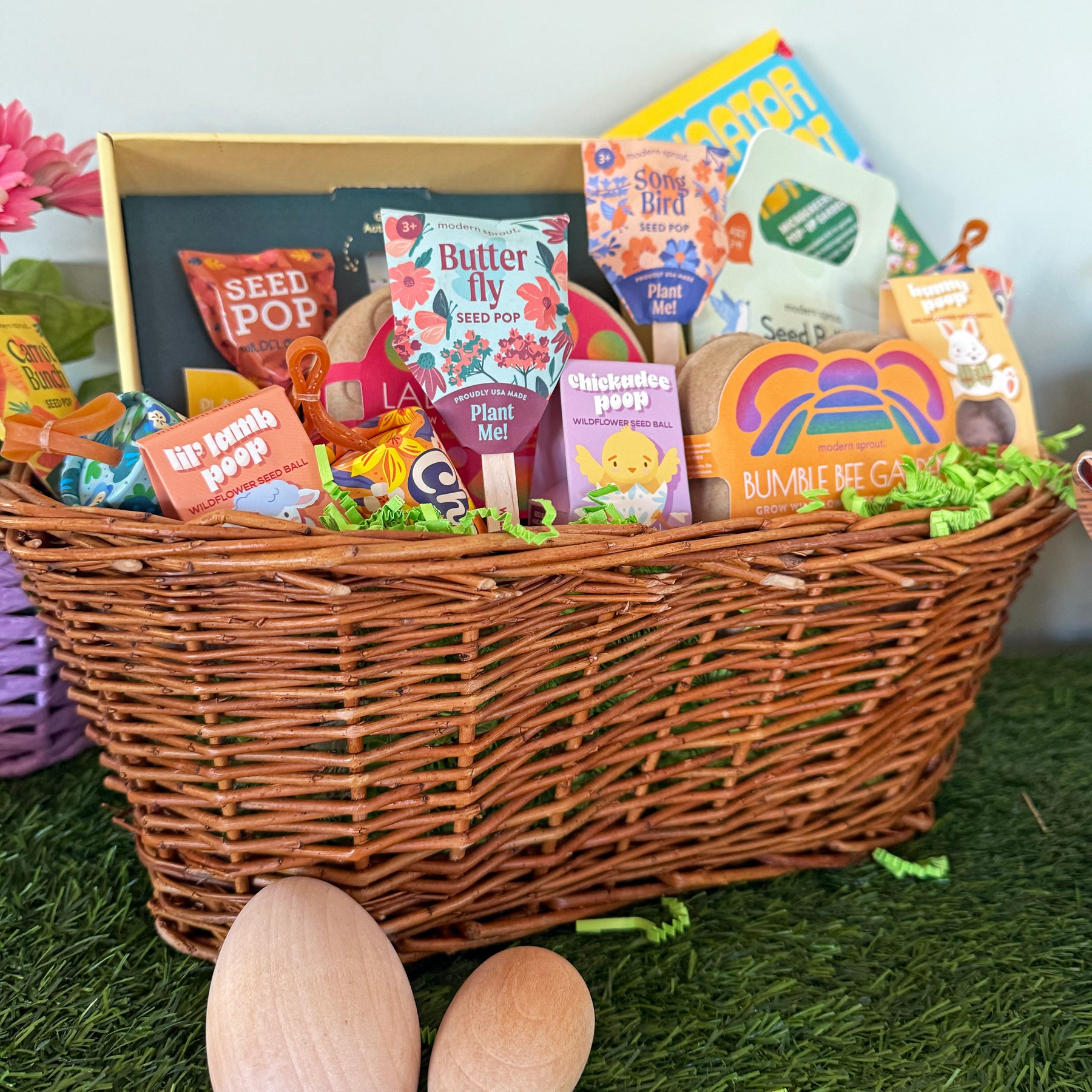 Woven Easter basket filled with seed packets, candy, and gardening items, surrounded by decorative grass and wooden eggs.