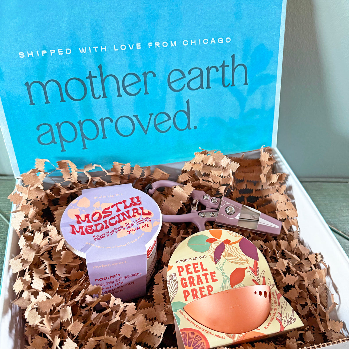 Limited edition gift box featuring a "Mostly Medicinal" lemon balm kit and "Peel Grate Prep" product, nestled in shredded paper.