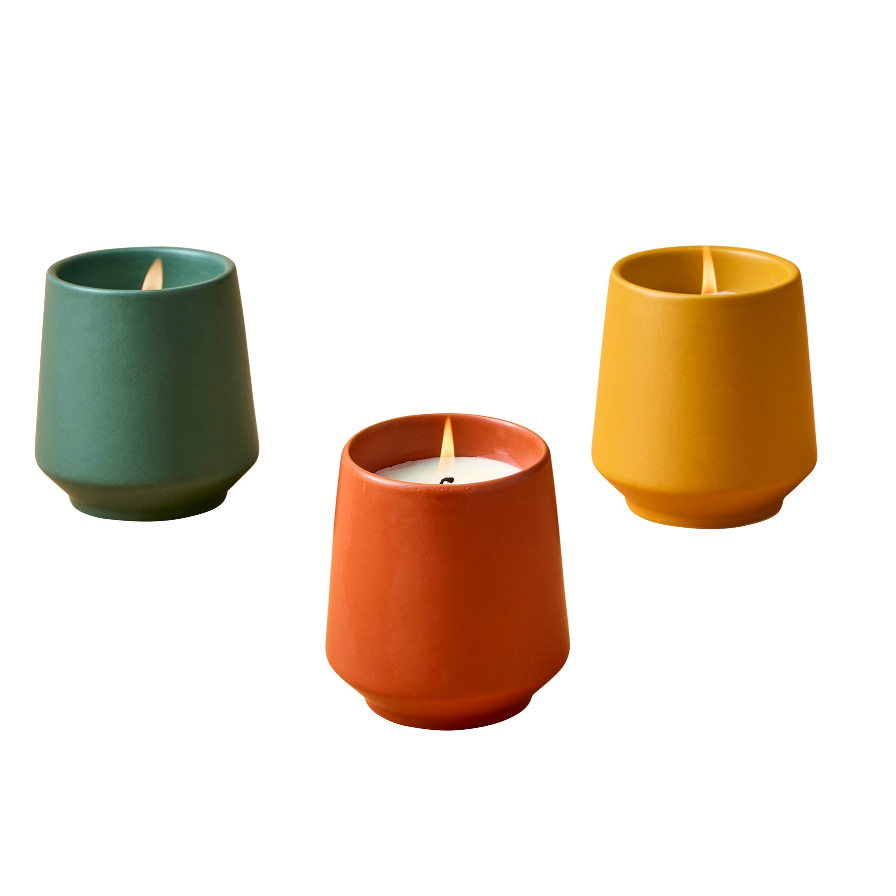 Three colorful ceramic candles in teal, orange, and yellow, each with a lit wick, arranged on a white background.