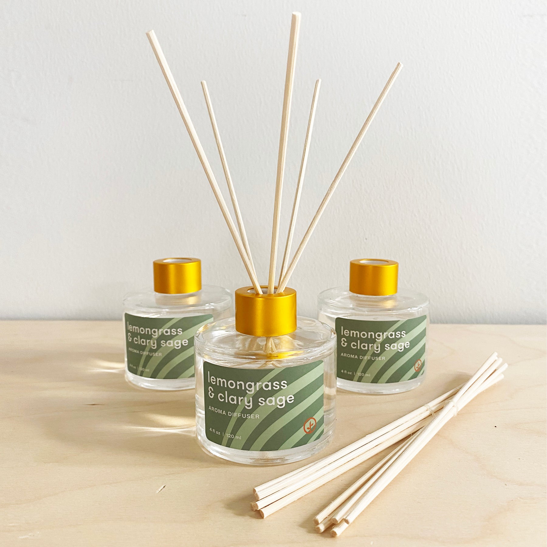 Three glass aroma diffusers with lemongrass and clary sage scent, featuring wooden reeds and gold caps, on a wooden surface.