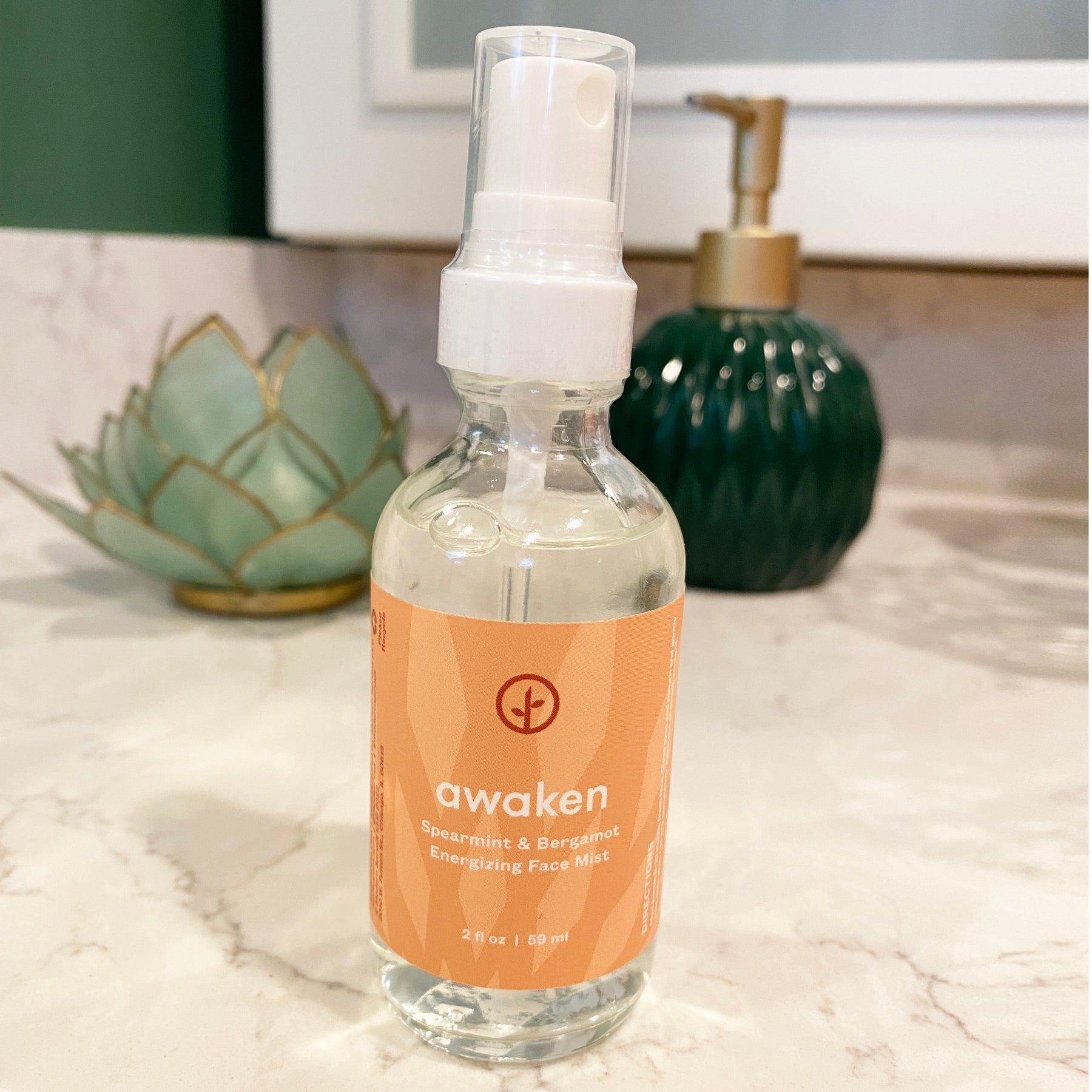 Three bottles of Shine Bright Face Mist featuring a refreshing spearmint and bergamot scent, displayed on a marble countertop.