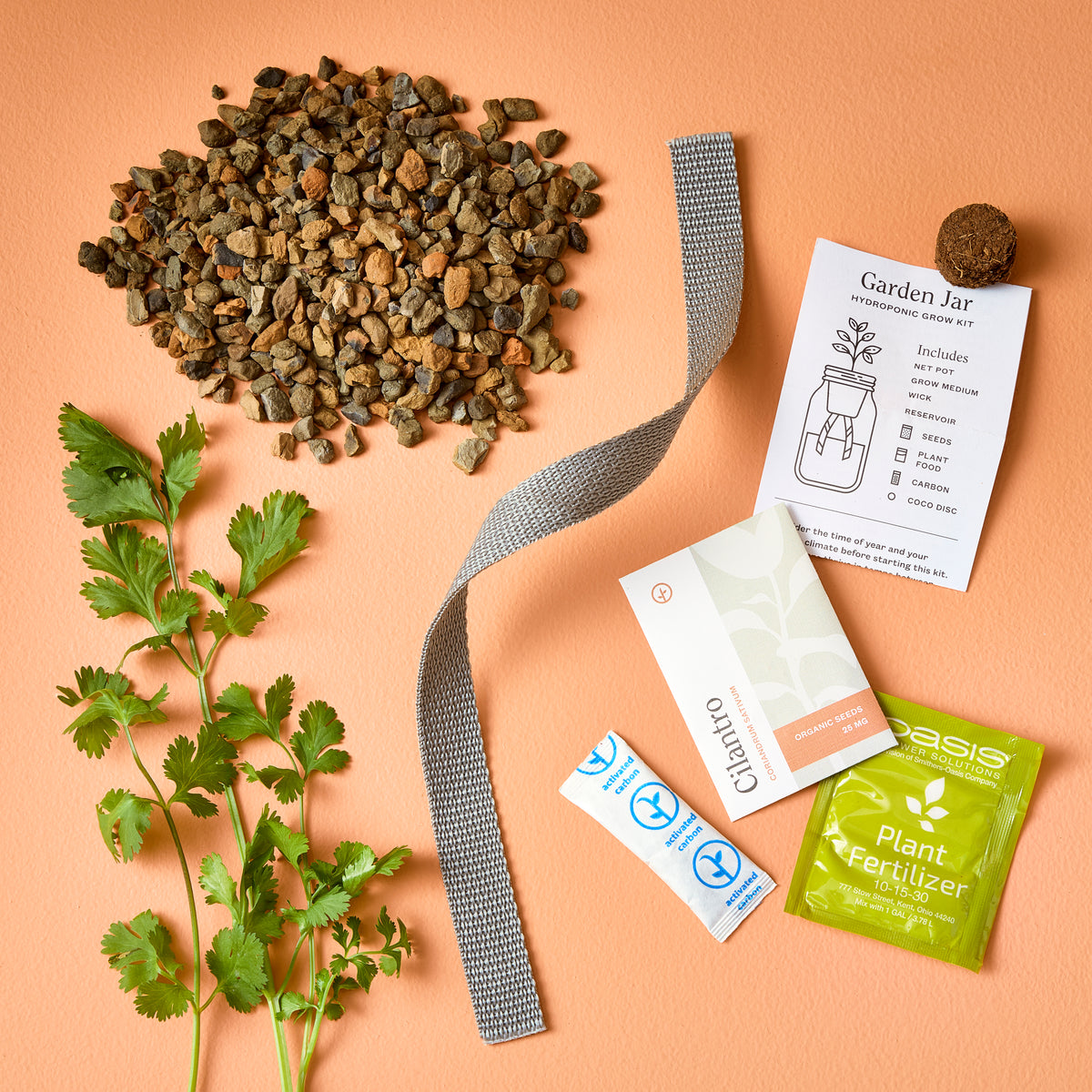 Green glass garden jars surrounded by soil, plant fertilizer, seeds, and fresh cilantro on a peach background.