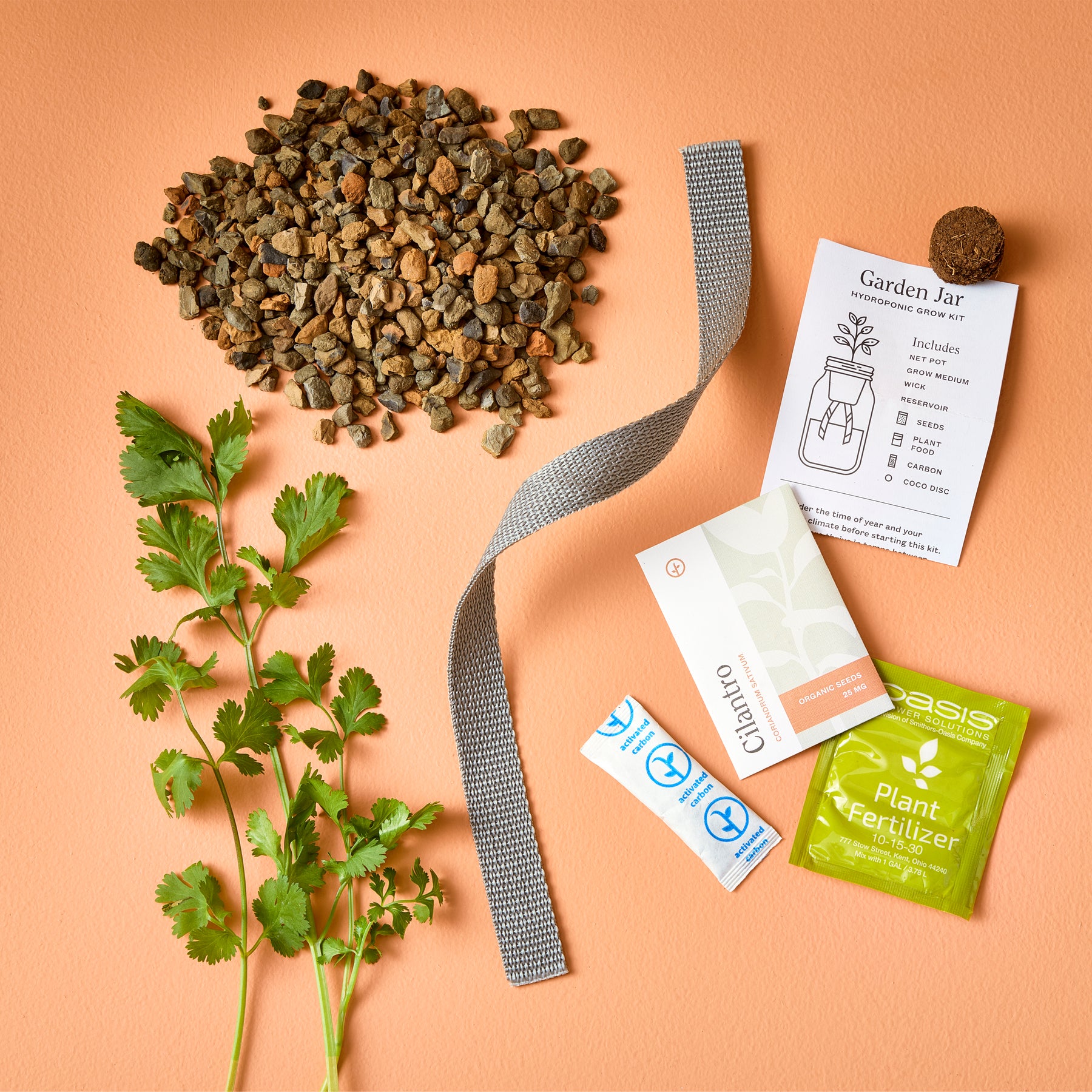Passive Hydroponic Replant Kit components including rocks, a plant label, fertilizer, and a sprig of cilantro on an orange background.