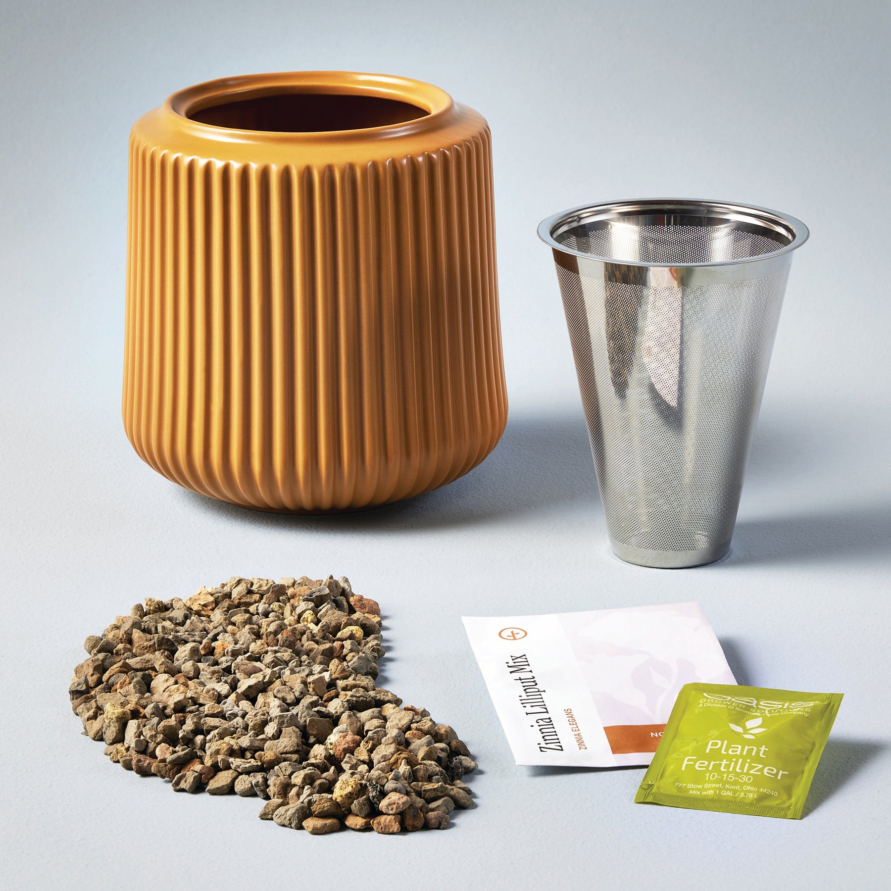 Flower grow kit featuring a ribbed orange planter, a metal mesh strainer, soil, and plant fertilizer packets.