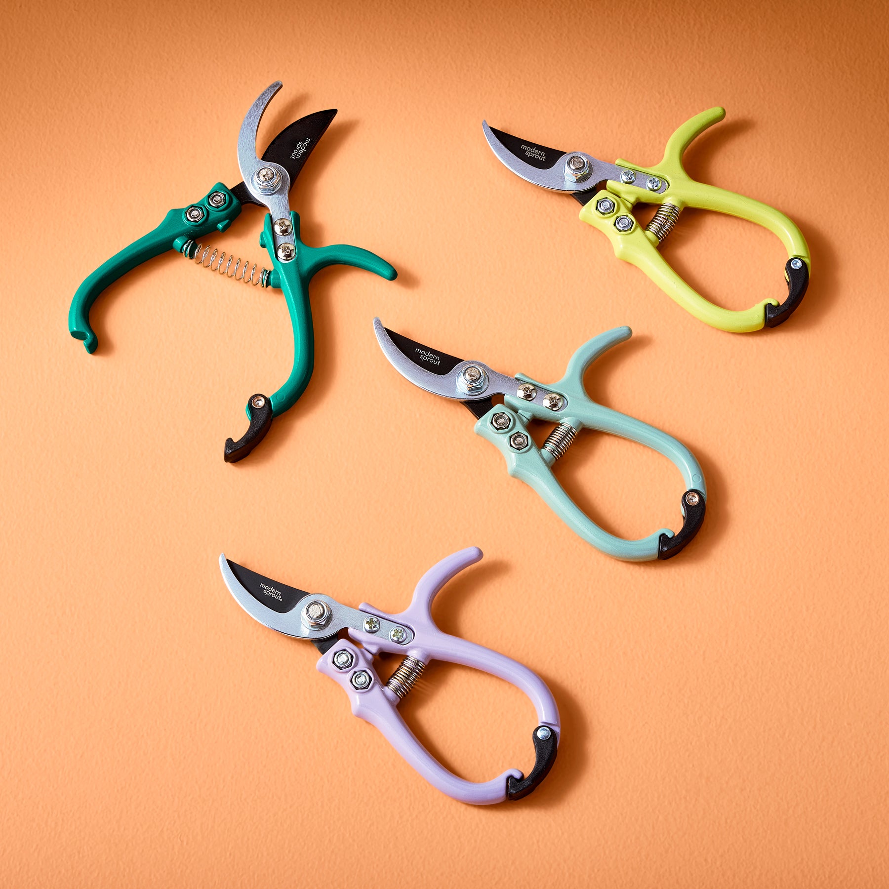 Colorful gardening shears and pruners in teal, yellow, mint, and lavender arranged on an orange background.