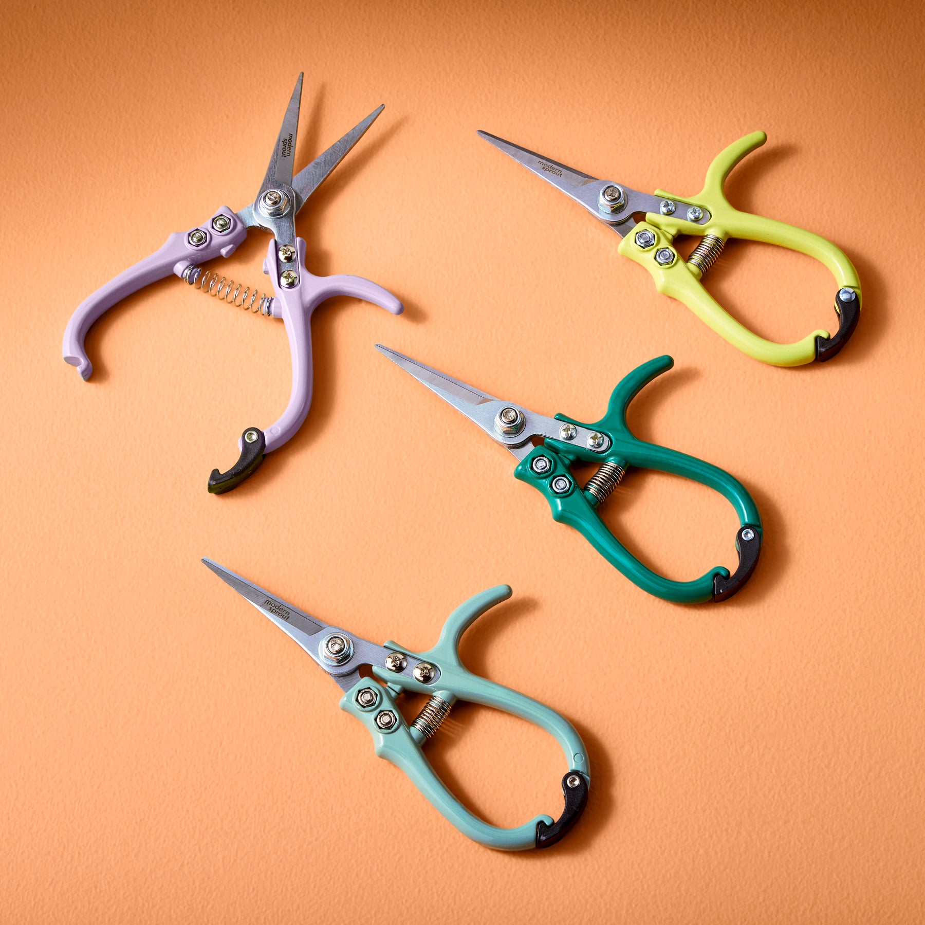 Colorful gardening shears and pruners in purple, yellow, green, and teal arranged on an orange background.