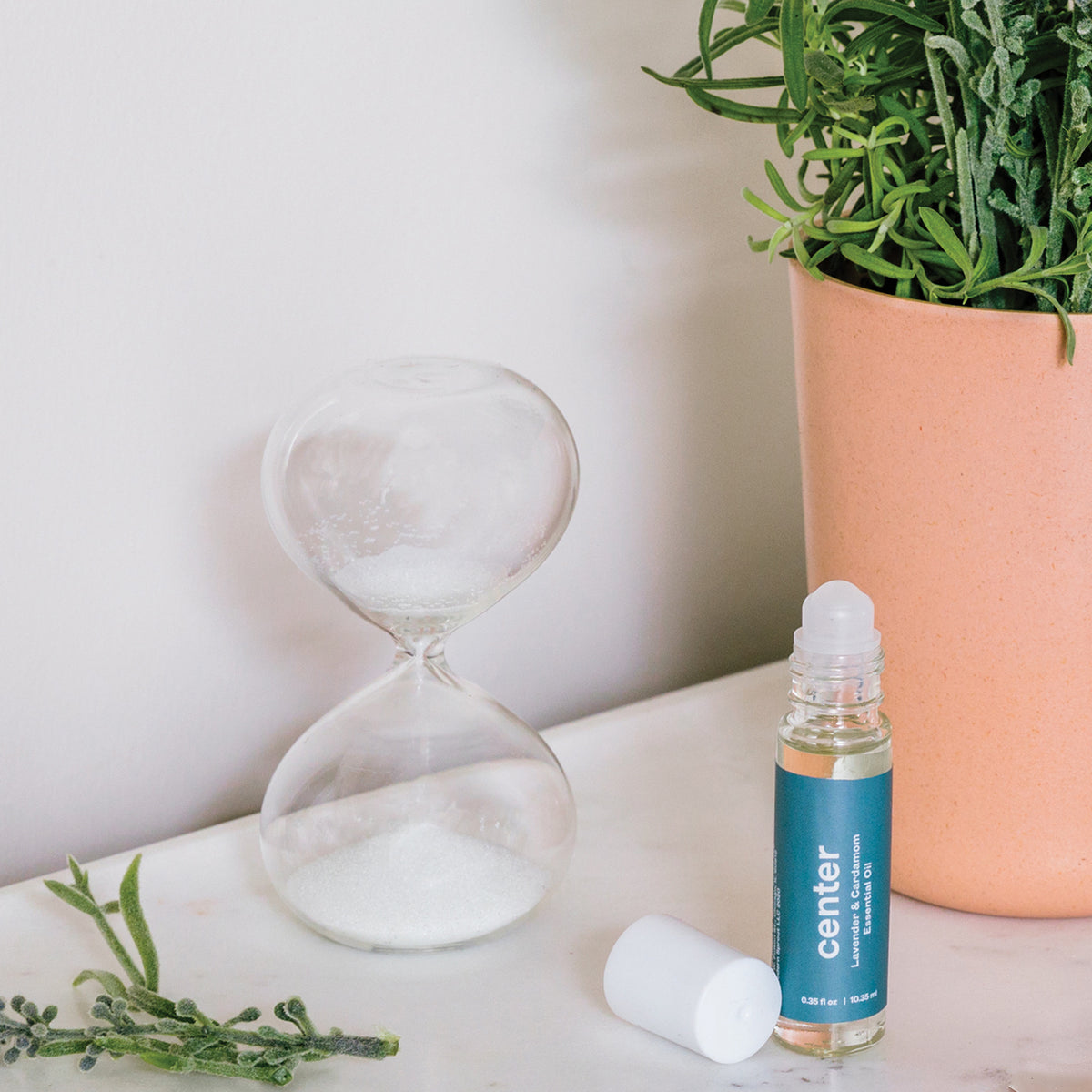 Three-pack of hourglasses with a roll-on essential oil bottle beside a potted plant, set against a neutral background.
