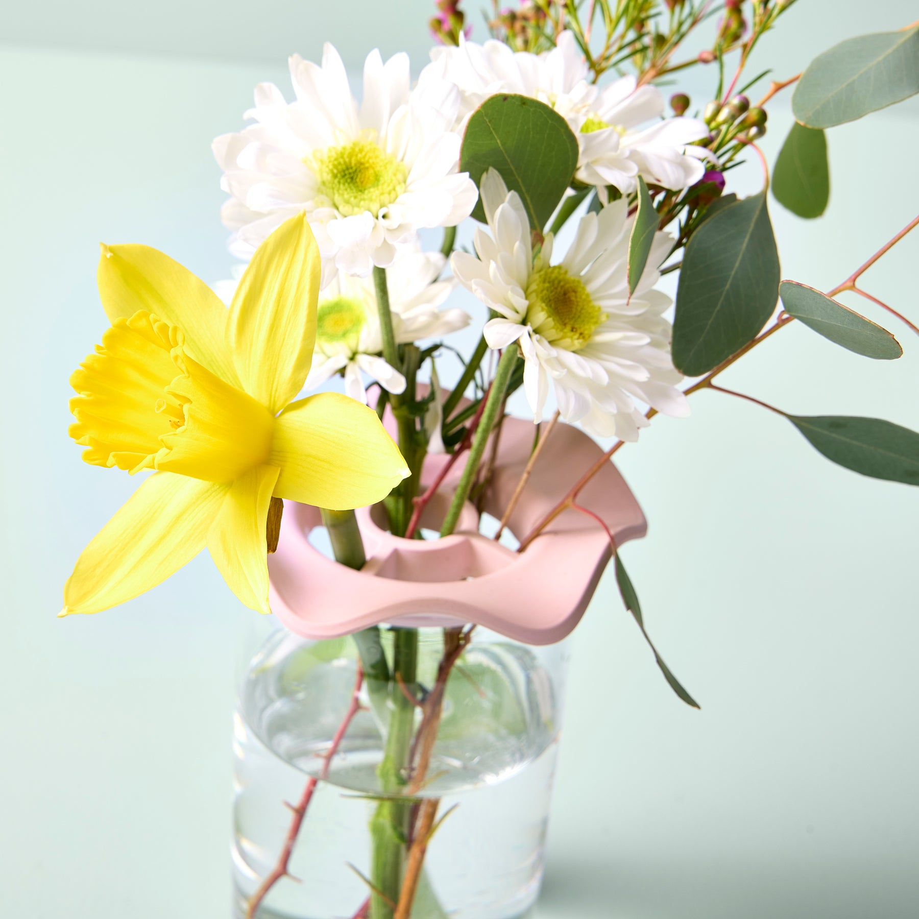 Two Botanical Keepers in use, holding fresh flowers, including a yellow daffodil and white daisies, in a clear vase.
