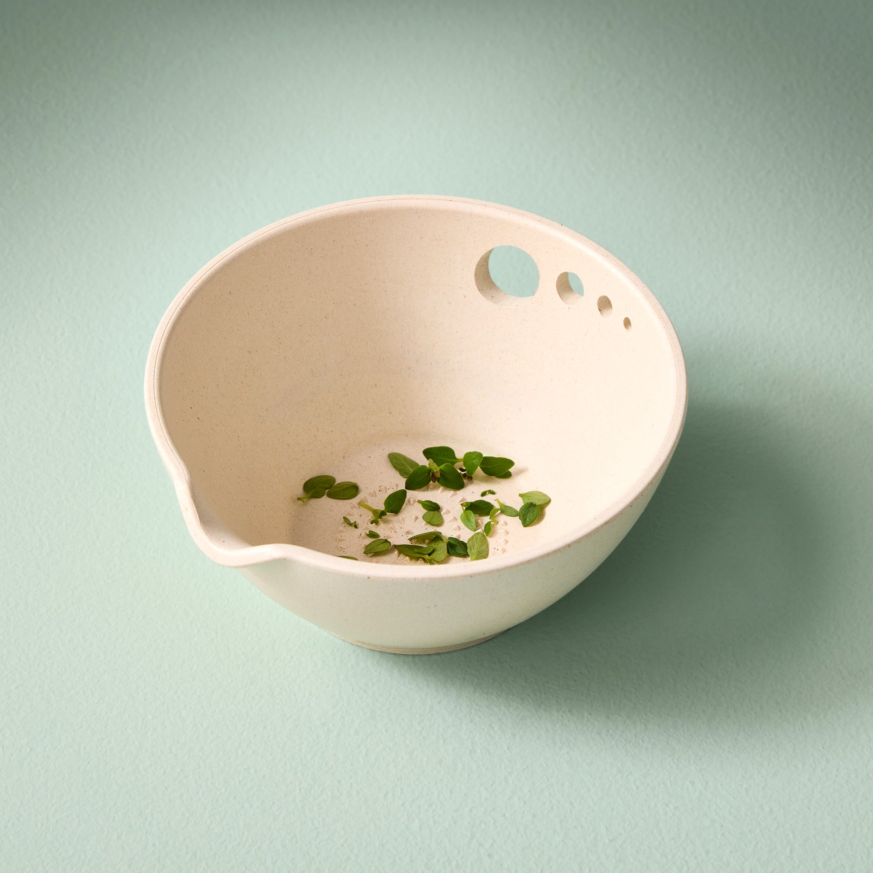 Natural-colored prep dish with a pouring spout, featuring small holes for easy grating and a few fresh herbs inside.