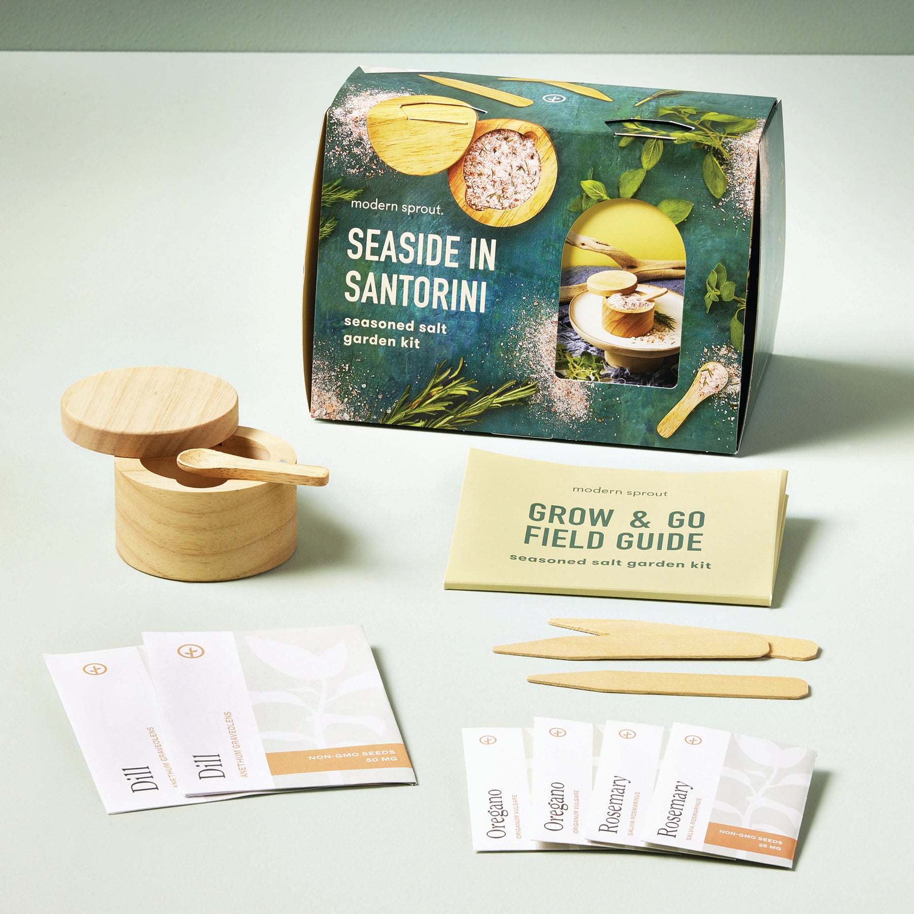 Seed collection kit featuring a box labeled "Seaside in Santorini," wooden containers, planting tools, and a field guide.