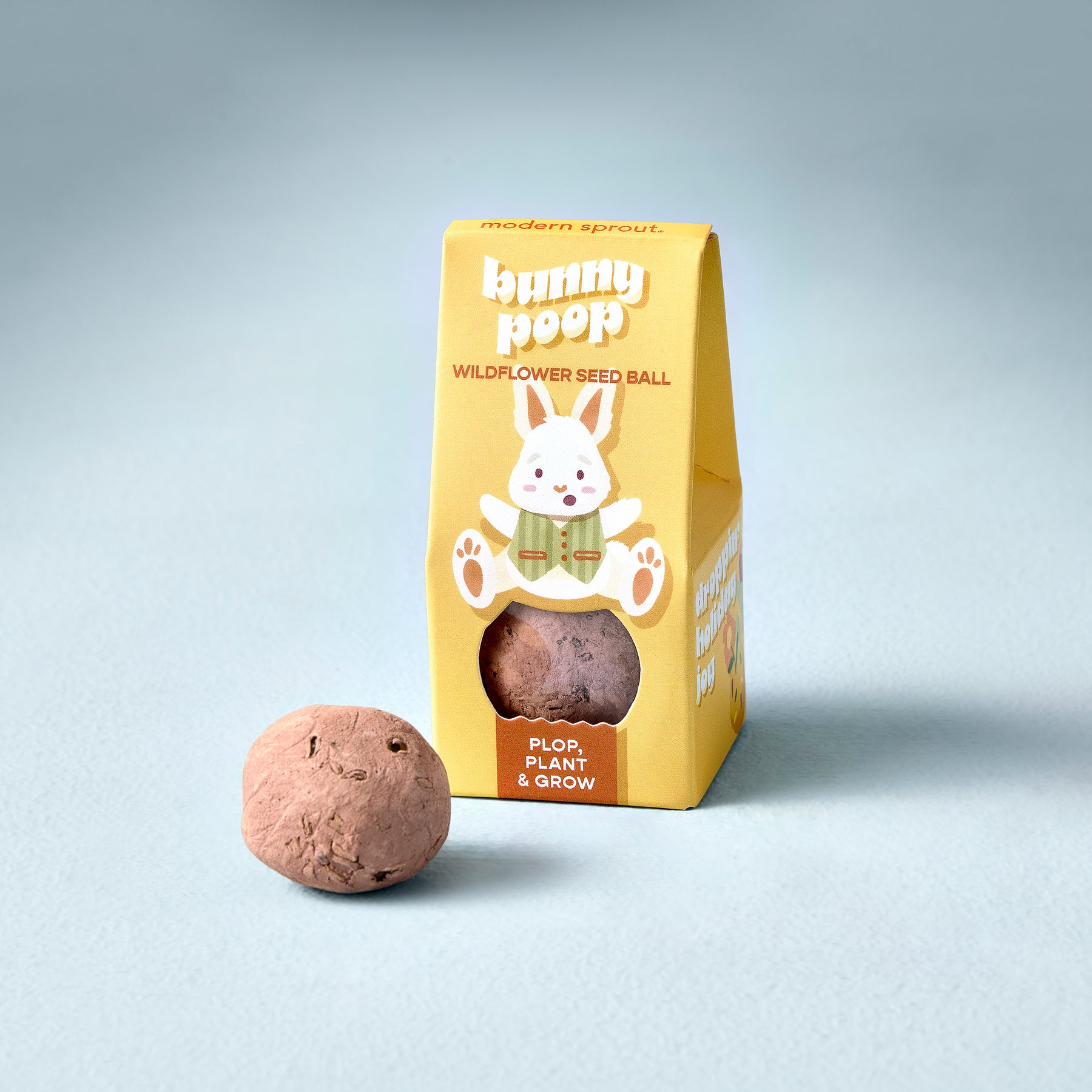Easter Plops wildflower seed ball next to a yellow box featuring a bunny design, promoting planting and growing.