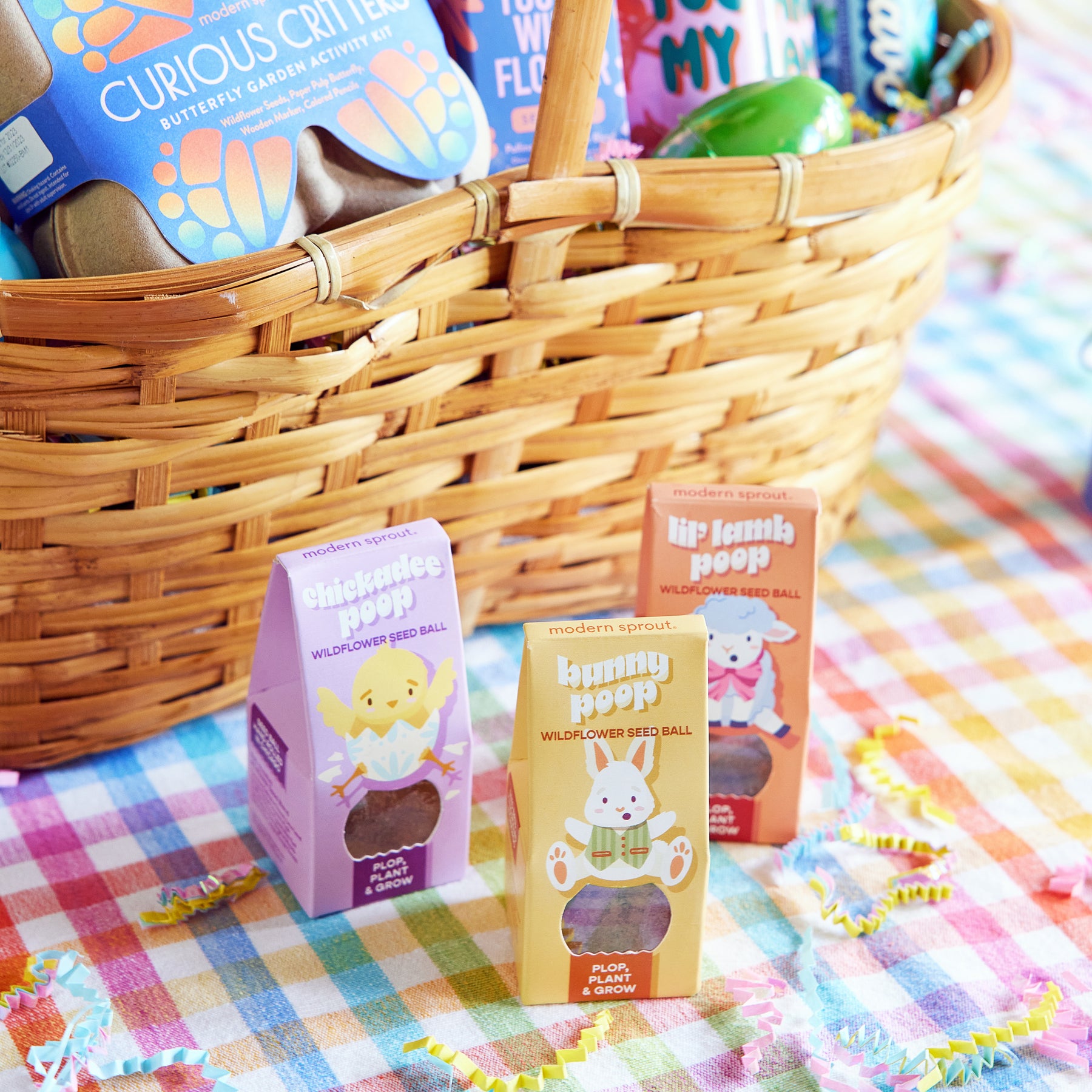 Colorful Easter Plops seed balls in playful packaging, displayed in a woven basket on a checkered tablecloth.