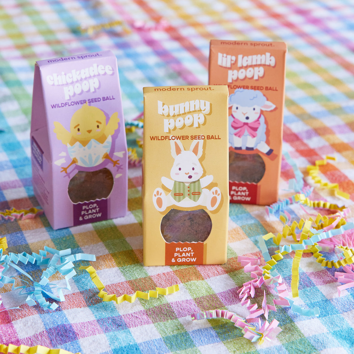 Colorful Easter Plops seed balls in playful packaging featuring a chick, bunny, and lamb on a checkered tablecloth.