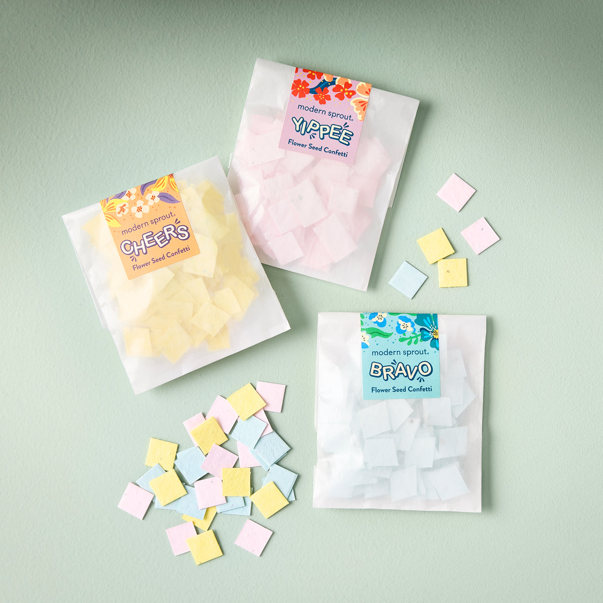 Three colorful seed paper confetti refill packs labeled Cheers, Yippee, and Bravo, with scattered confetti pieces on a light green background.