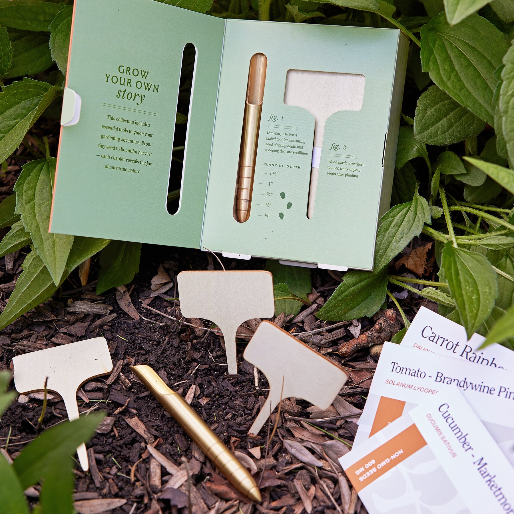 Seed library kit featuring planting depth guide, wooden plant markers, and a gold pen, set among garden soil and foliage.