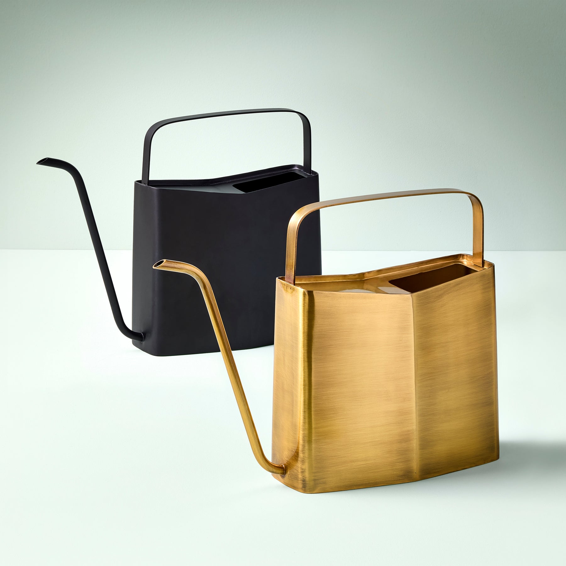 Two modern watering cans, one black and one gold, displayed against a light green background, showcasing sleek designs.