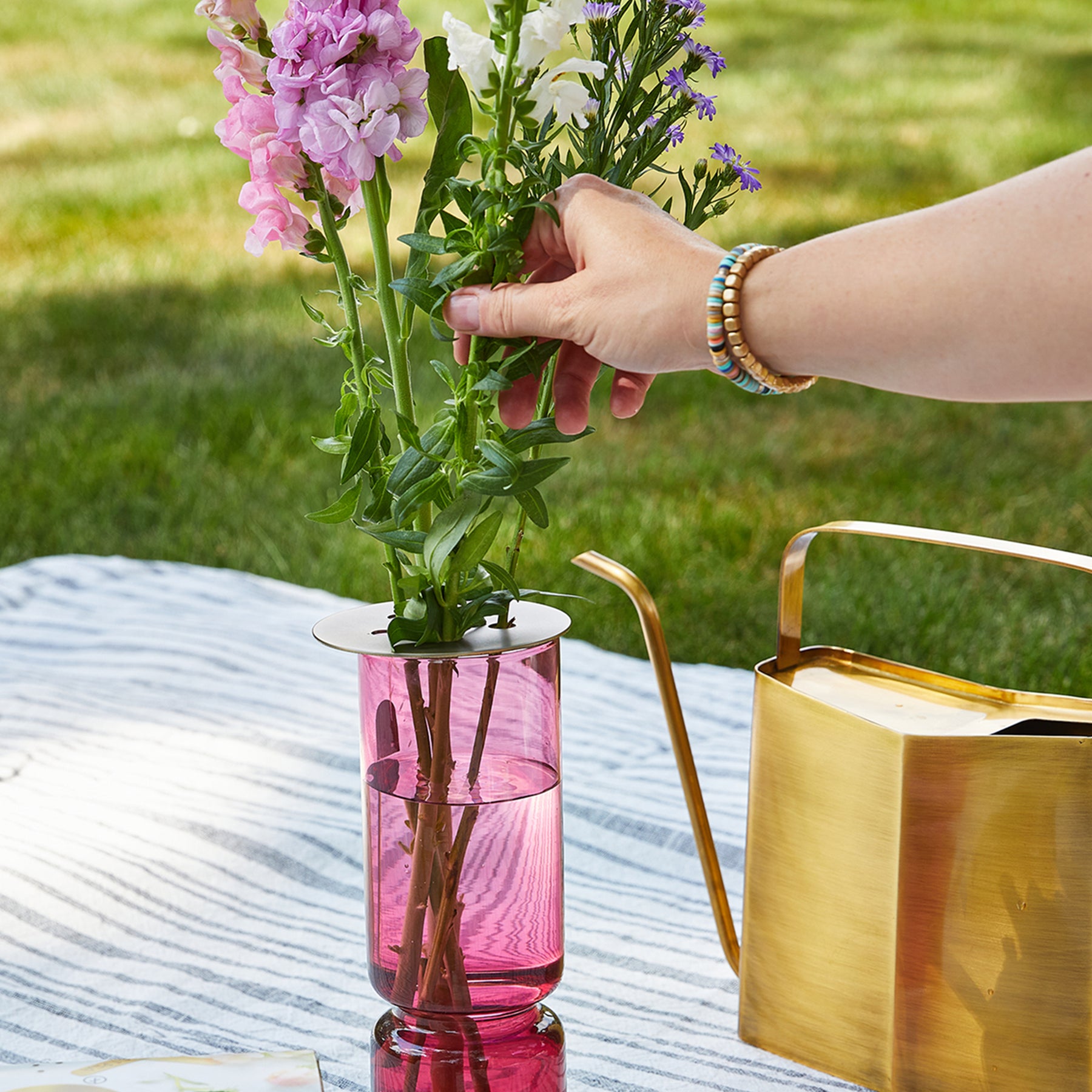 Brass flower frog placed in a pink vase, supporting fresh flowers while a hand adjusts the arrangement outdoors.