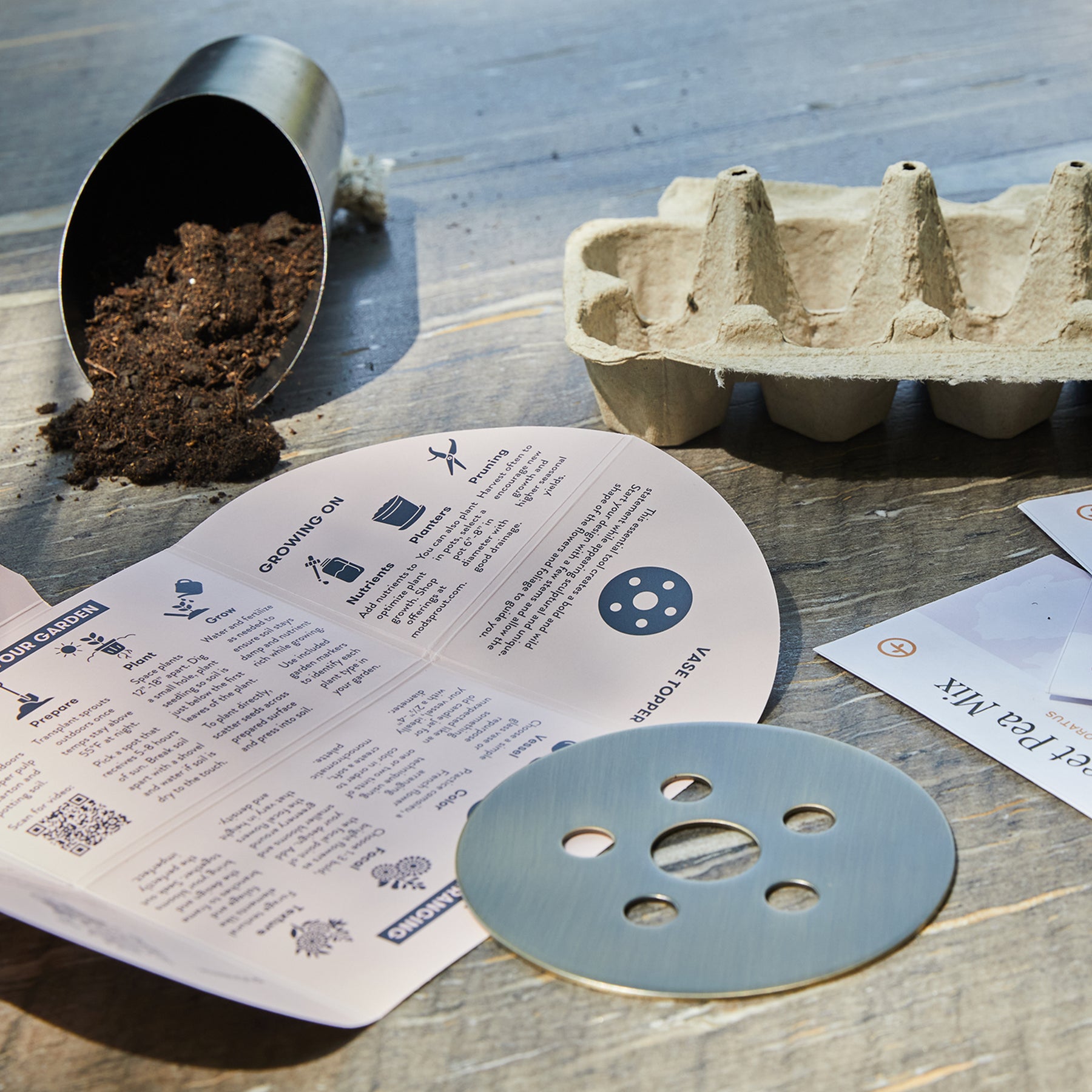 Brass flower frog on a wooden surface with gardening supplies, including soil, seed trays, and instructions.