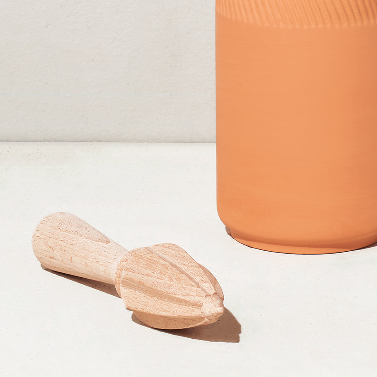 Natural wood citrus reamer beside a terracotta-colored container on a light surface, ideal for juicing citrus fruits.