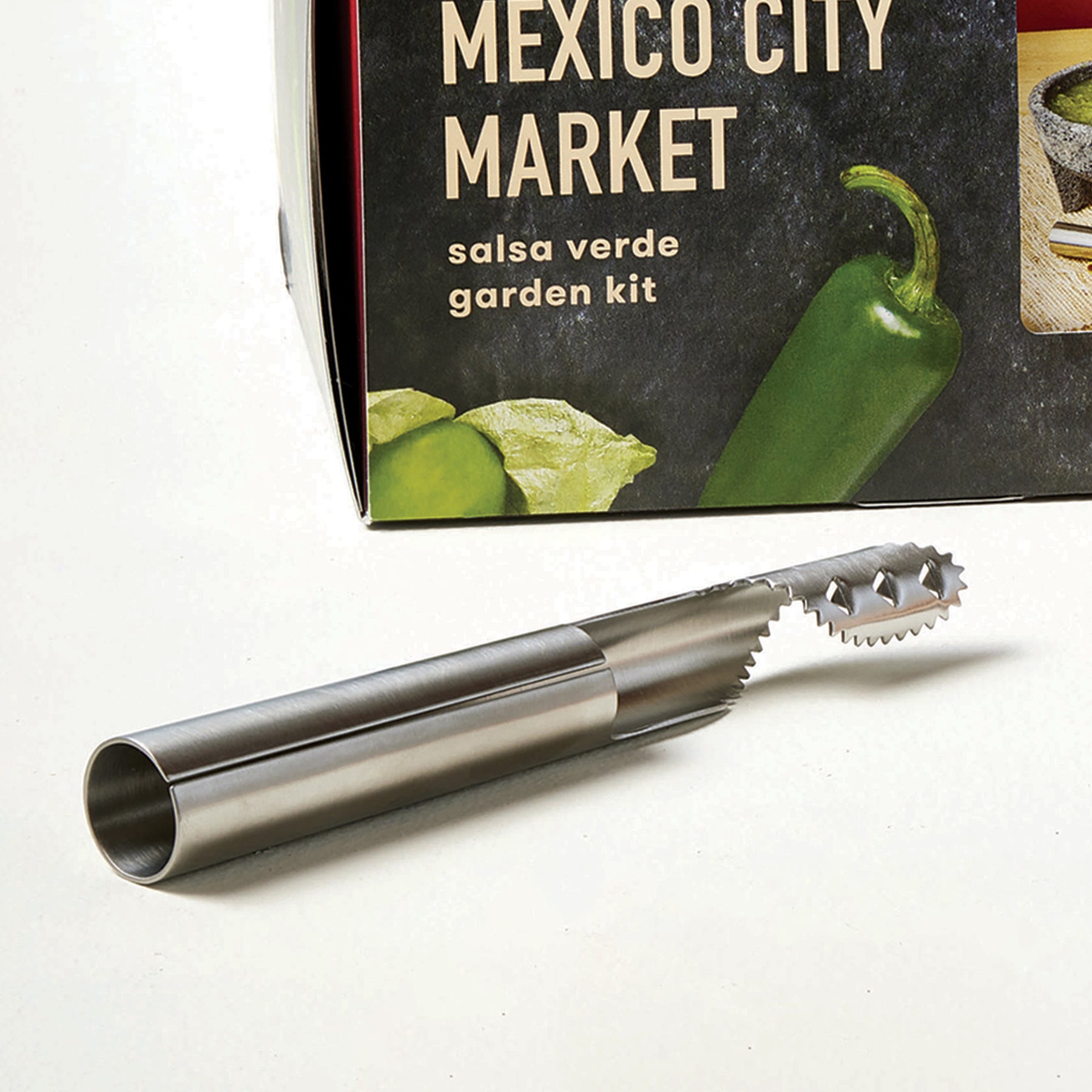 Stainless steel pepper de-seeder tool with a spiral tip, placed next to a colorful product box for a salsa verde garden kit.