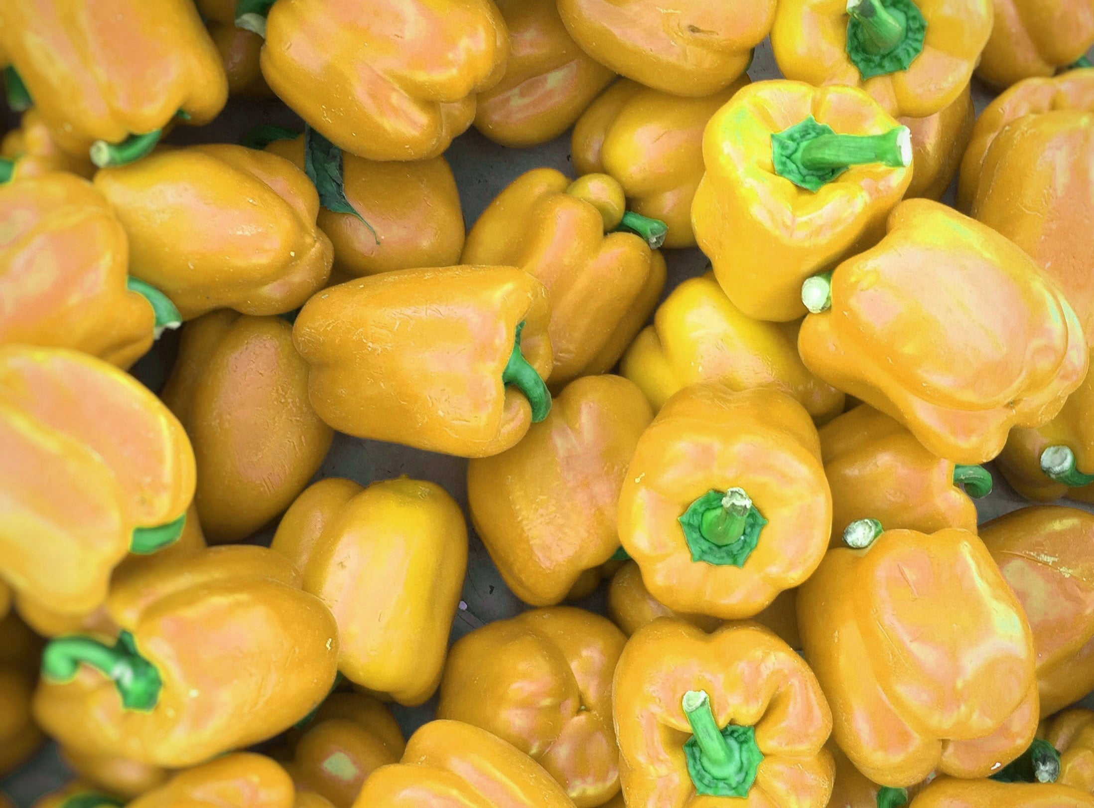 Close-up of yellow bell peppers with green stems, highlighting vibrant colors and fresh, glossy texture.