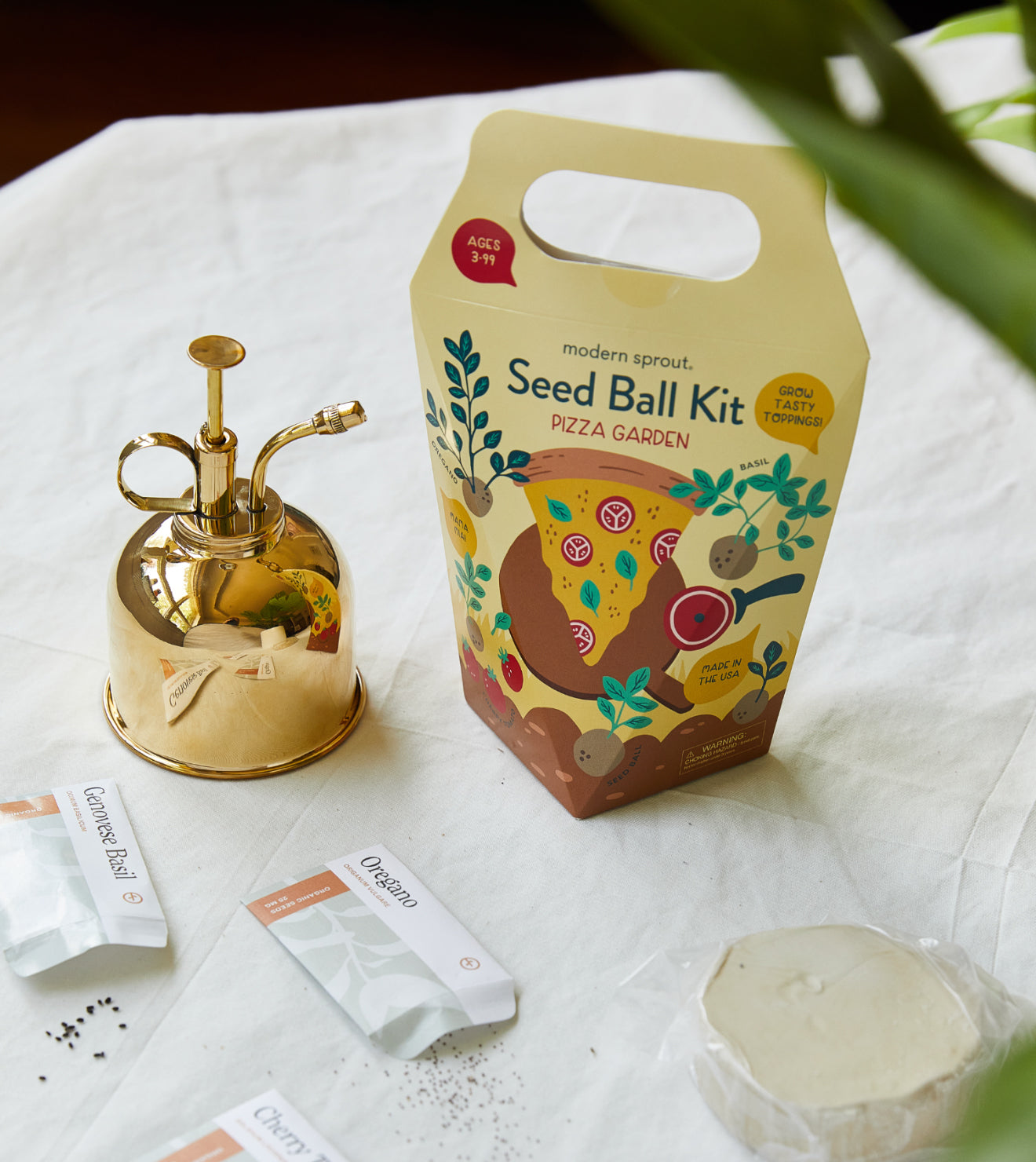 Hydroponic seed ball kit in colorful packaging, with basil and oregano seed packets, on a white table.