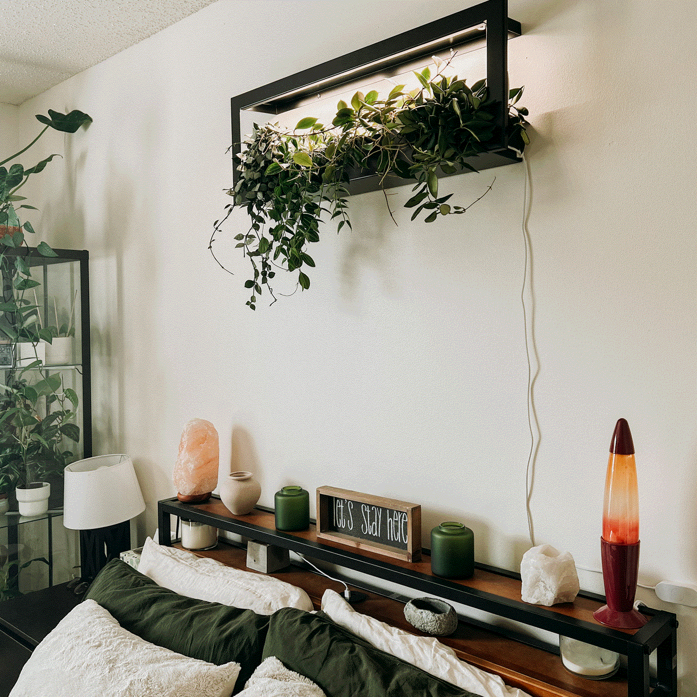 Wall-mounted hydroponic garden with lush green plants in a modern black frame, above a cozy bedroom setup.