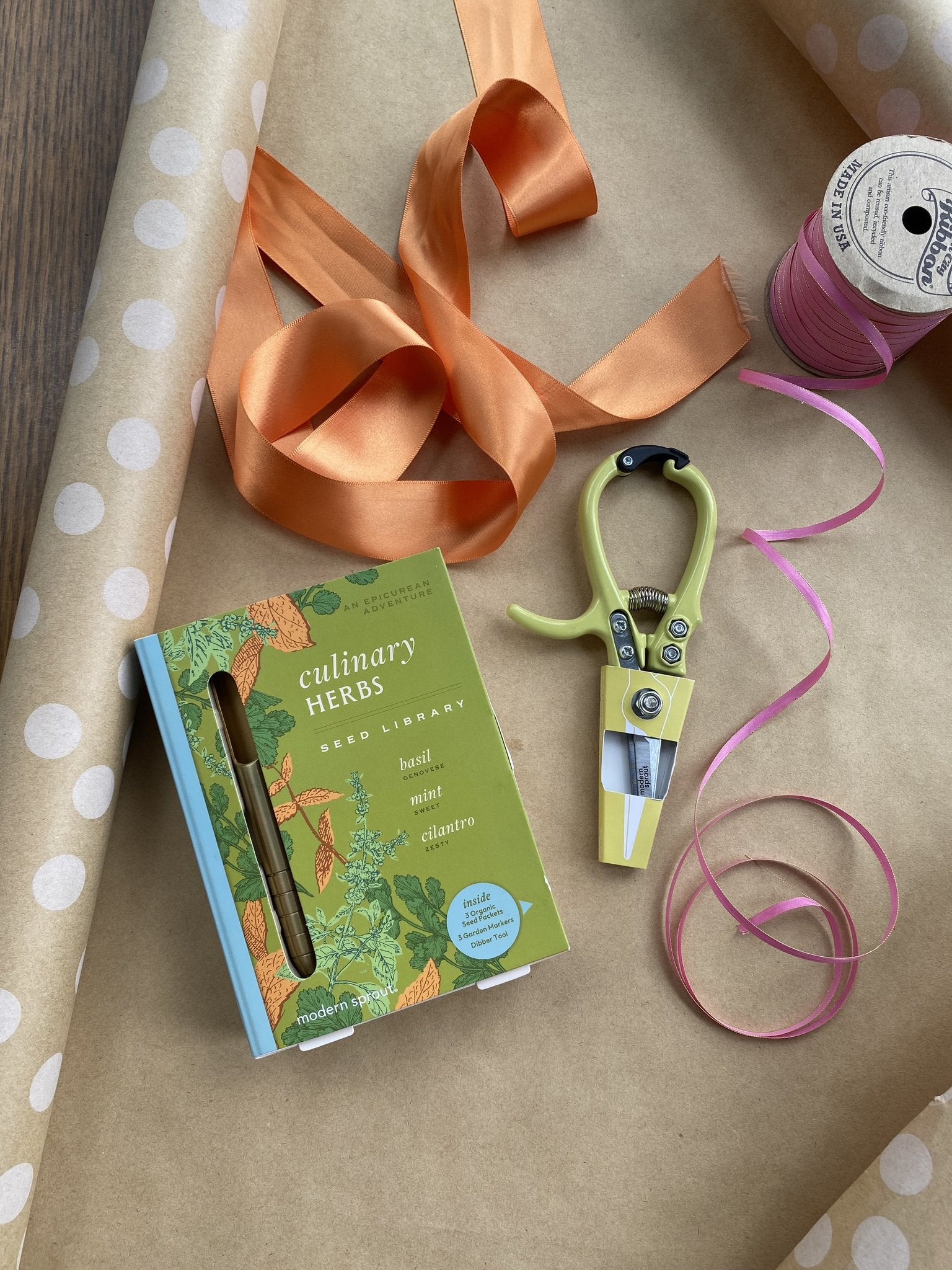 Culinary herbs seed library book next to gardening shears and colorful ribbons on a polka dot background.