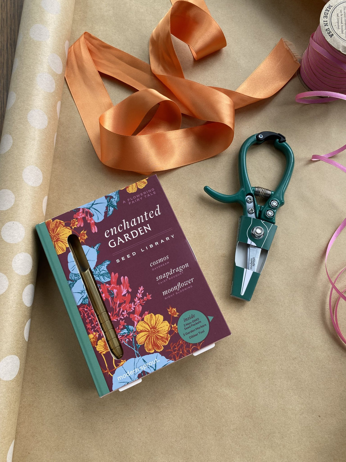 Seed library box titled "Enchanted Garden" alongside green gardening shears and decorative ribbons on a craft surface.