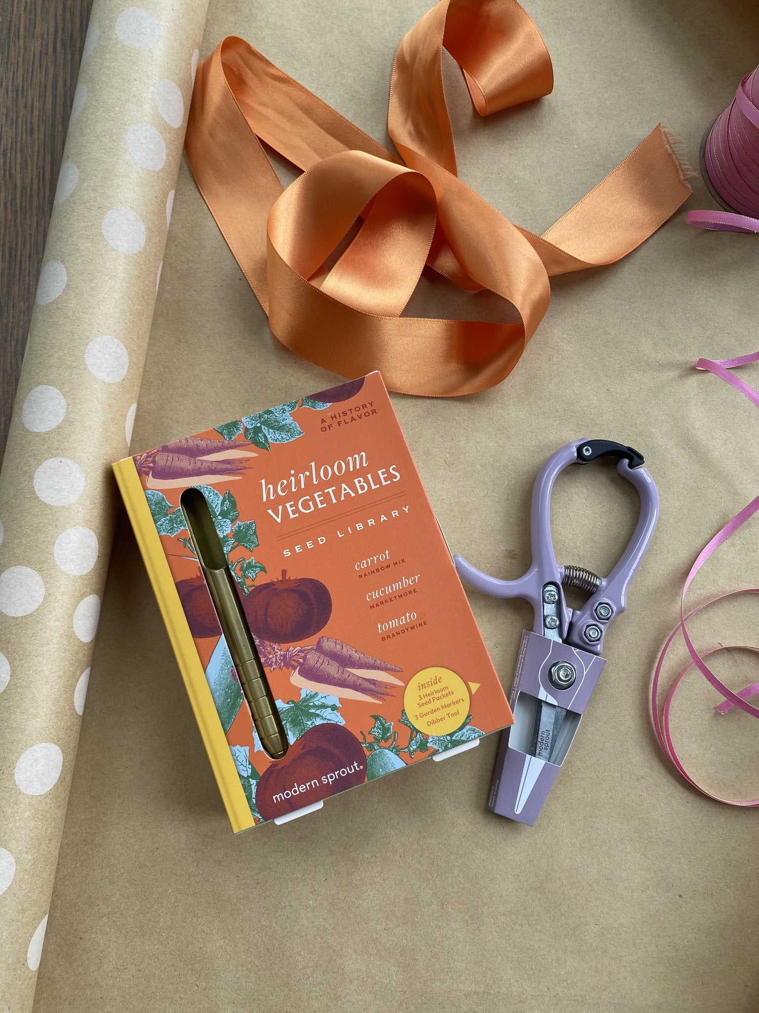 Heirloom vegetable seed library box next to gardening shears and decorative ribbons on brown wrapping paper.