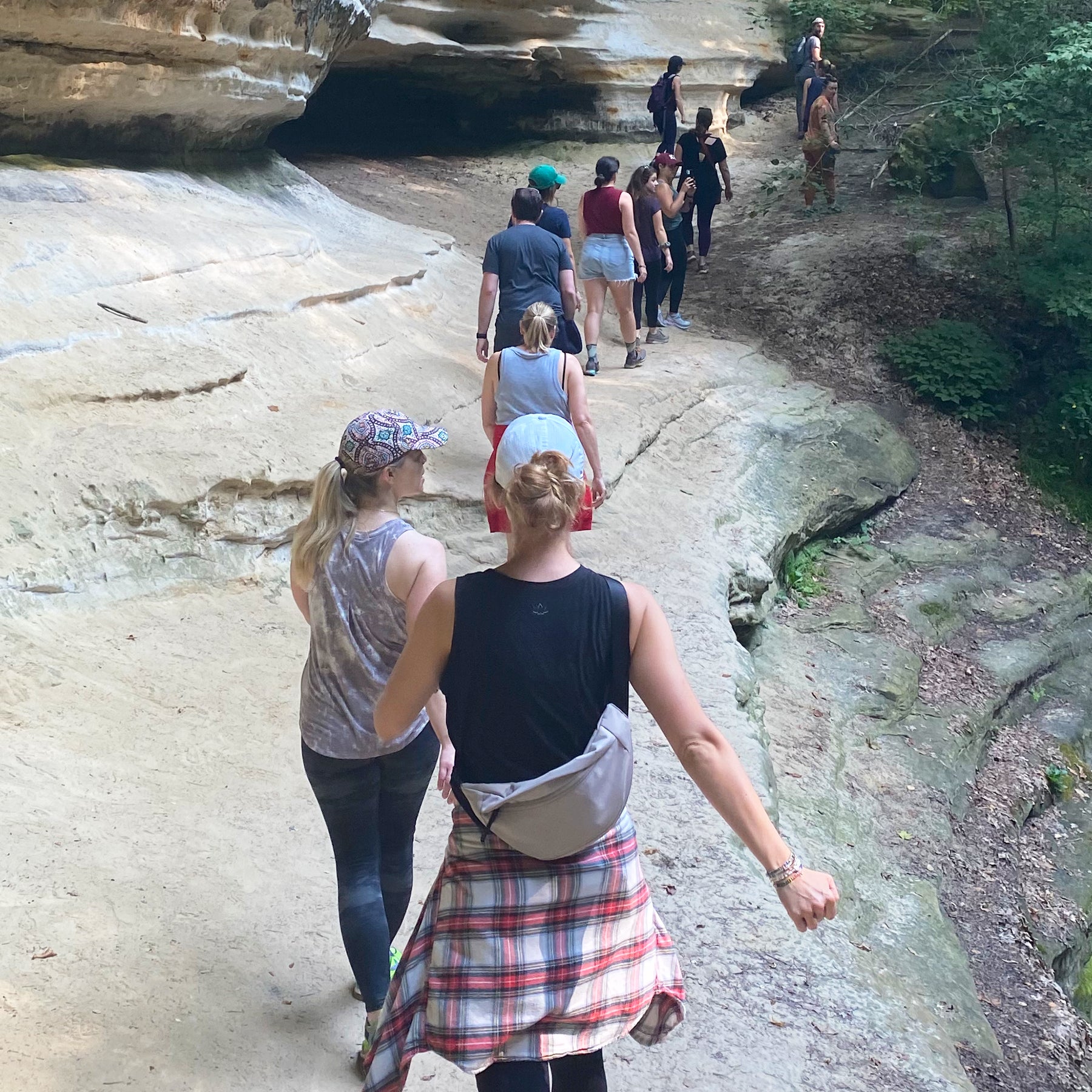 Group of hikers on a rocky trail in a lush forest, wearing casual outdoor gear, enjoying a nature walk.