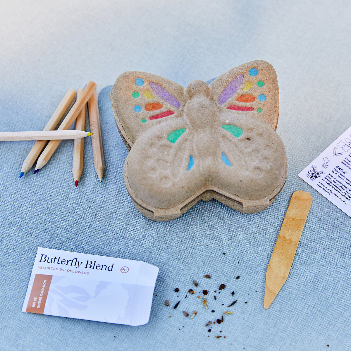 Curious Critters Garden Kit featuring a butterfly-shaped seed starter, colored pencils, planting stick, and wildflower seeds.