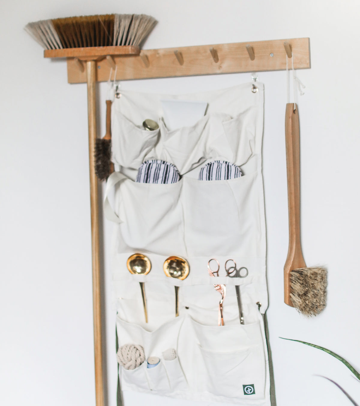 Hanging organizer apron with multiple pockets, tools, and a broom, mounted on a wall for easy access and storage.