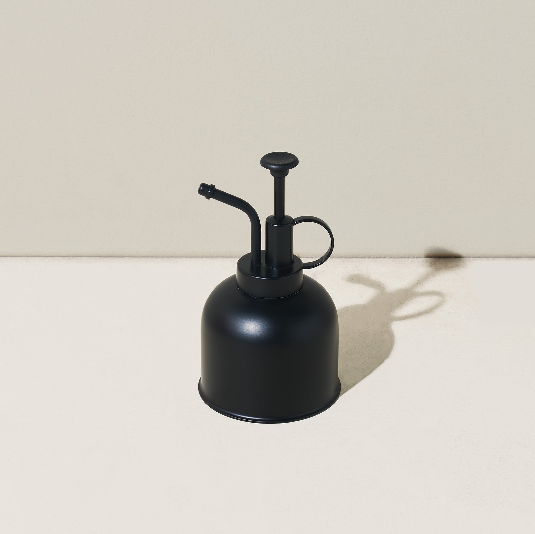Black metal watering can with a long spout and a pump handle, designed for precise plant care.