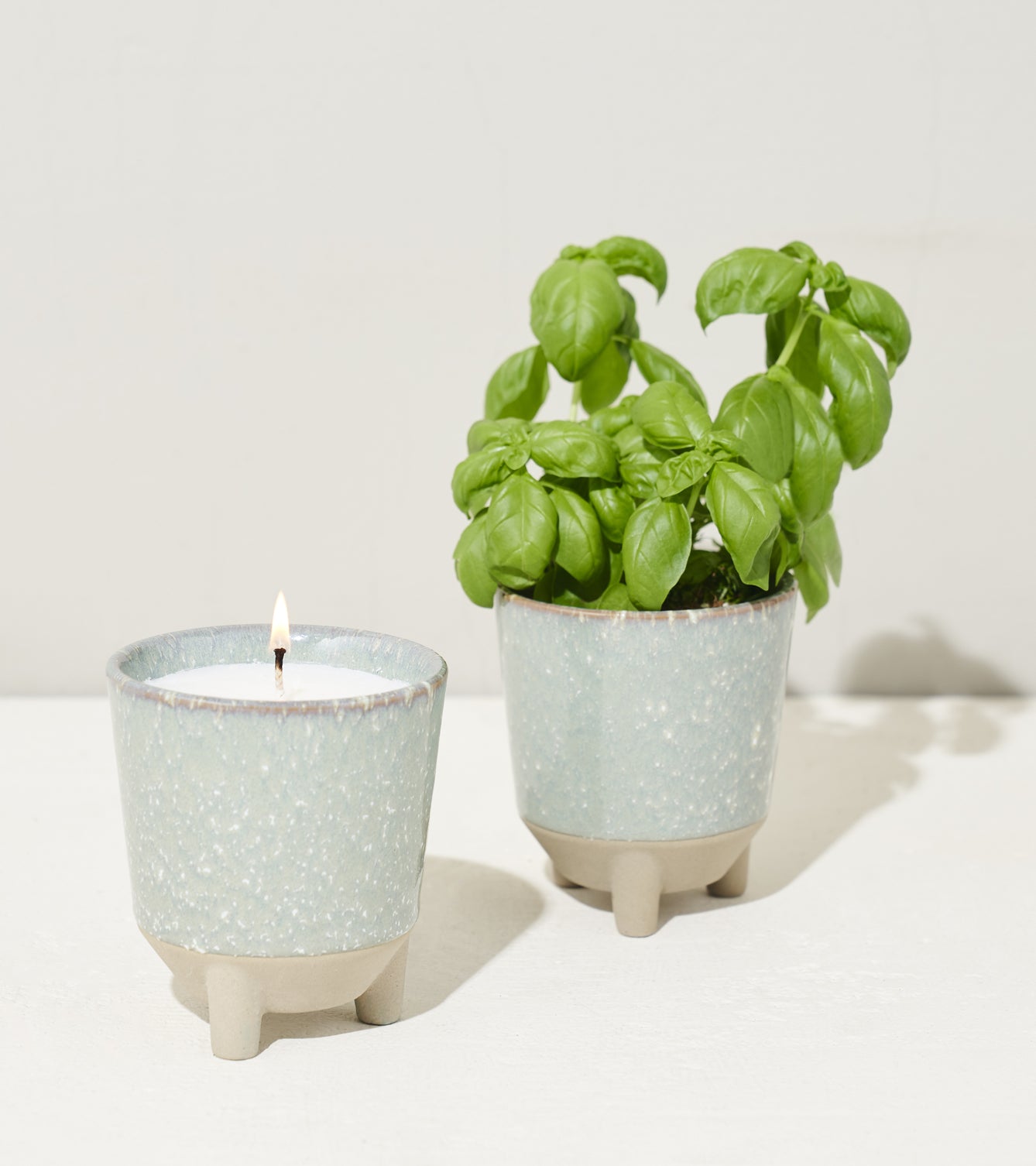 Two ceramic pots: one with a lit candle and the other with vibrant basil plants, showcasing a stylish Glow & Grow Kit.