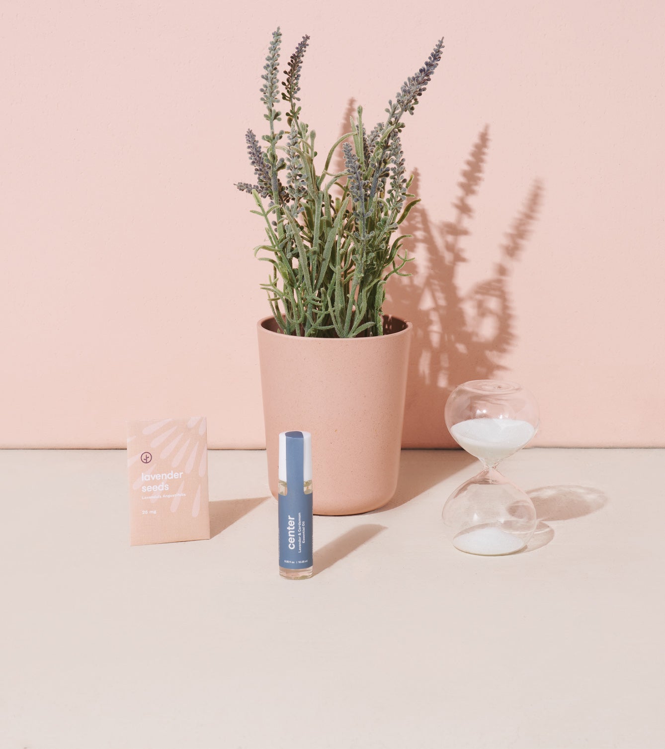 Mindful meditation kit featuring lavender seeds, a calming essential oil, and an hourglass next to a potted plant.