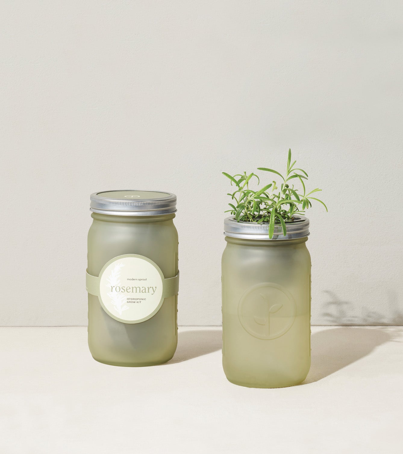 Green glass garden jars with rosemary, featuring a sleek design and metal lids, ideal for indoor herb gardening.