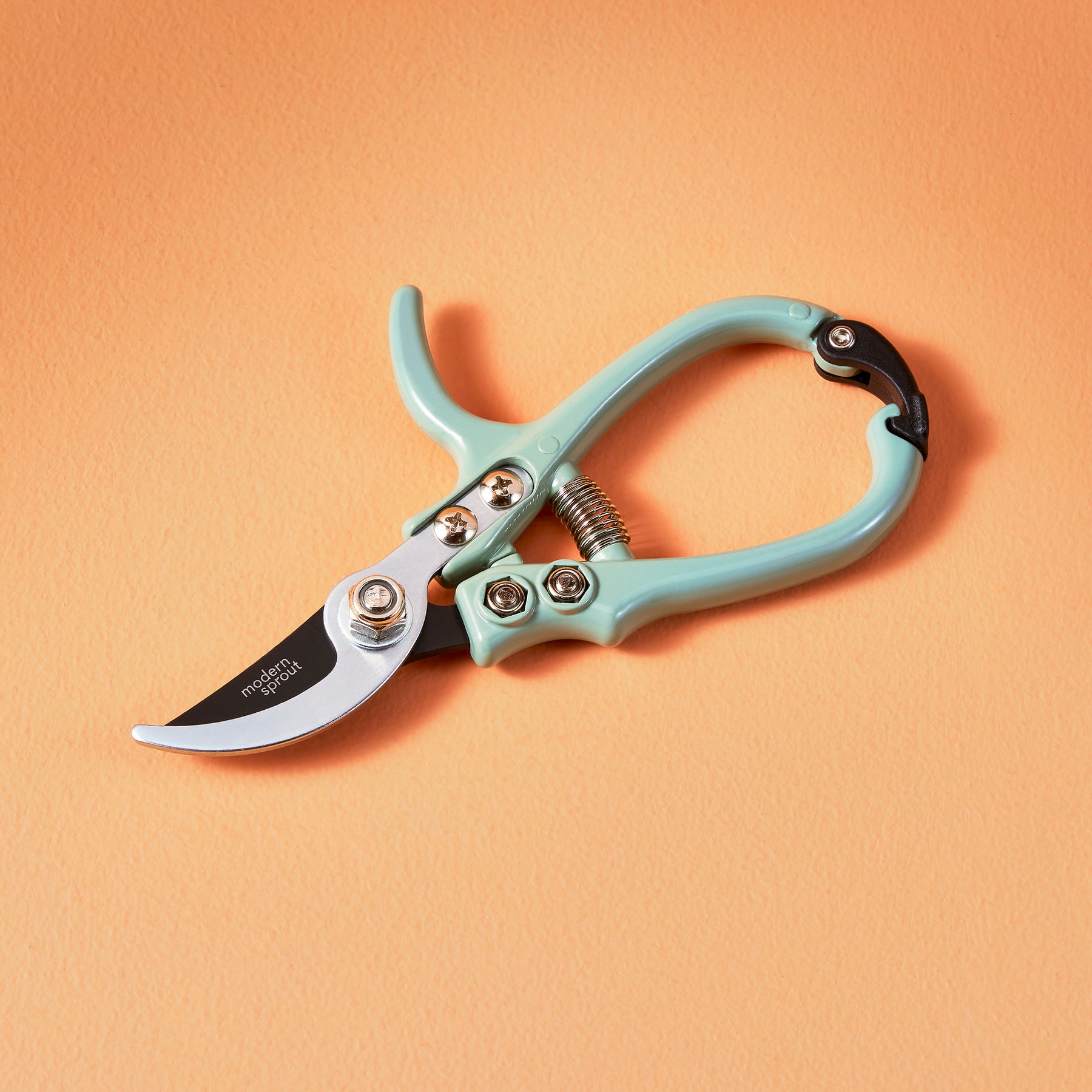Mint green gardening shears with a curved blade and ergonomic handle, resting on a peach background.