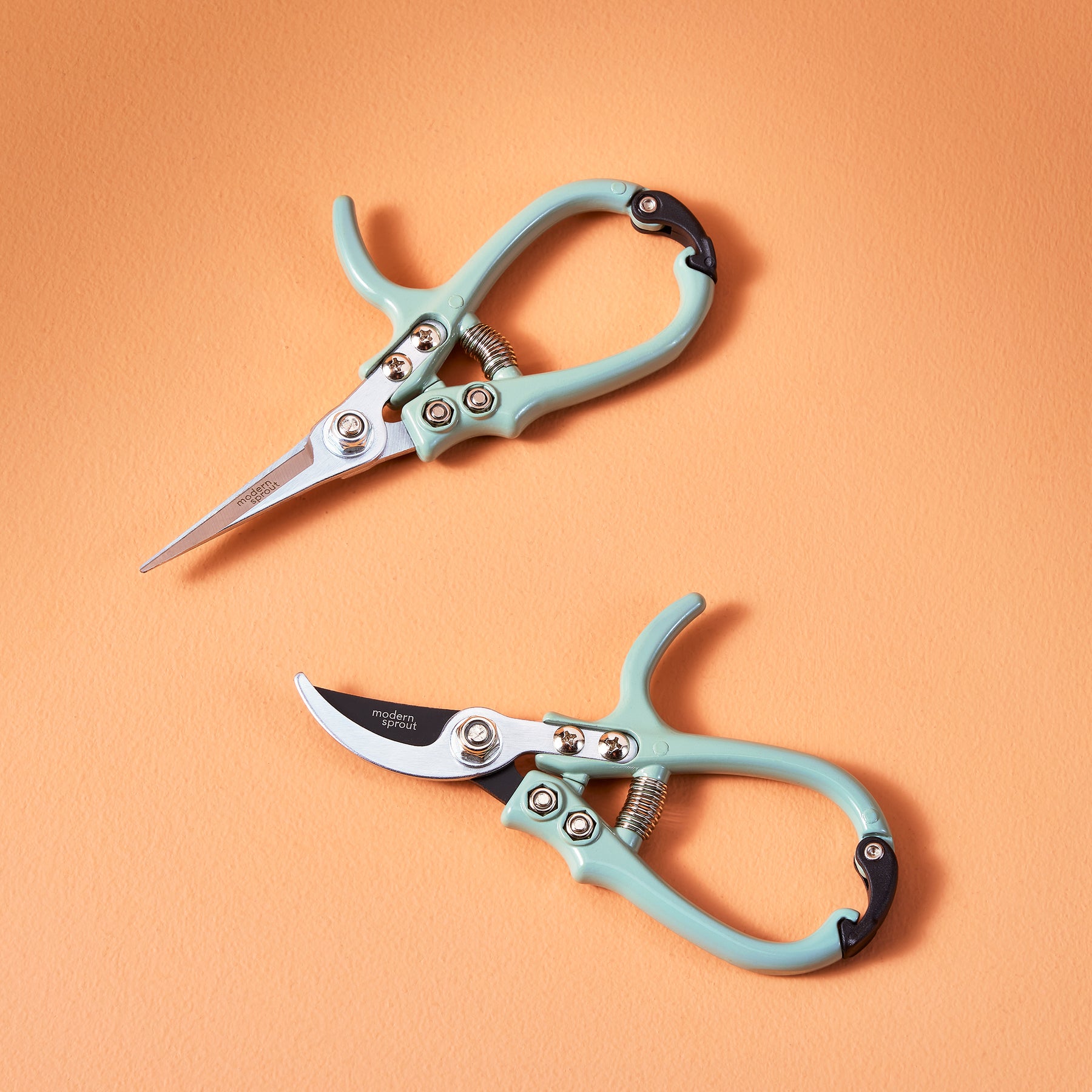 Two gardening shears and pruners with mint green handles on an orange background, showcasing their ergonomic design.