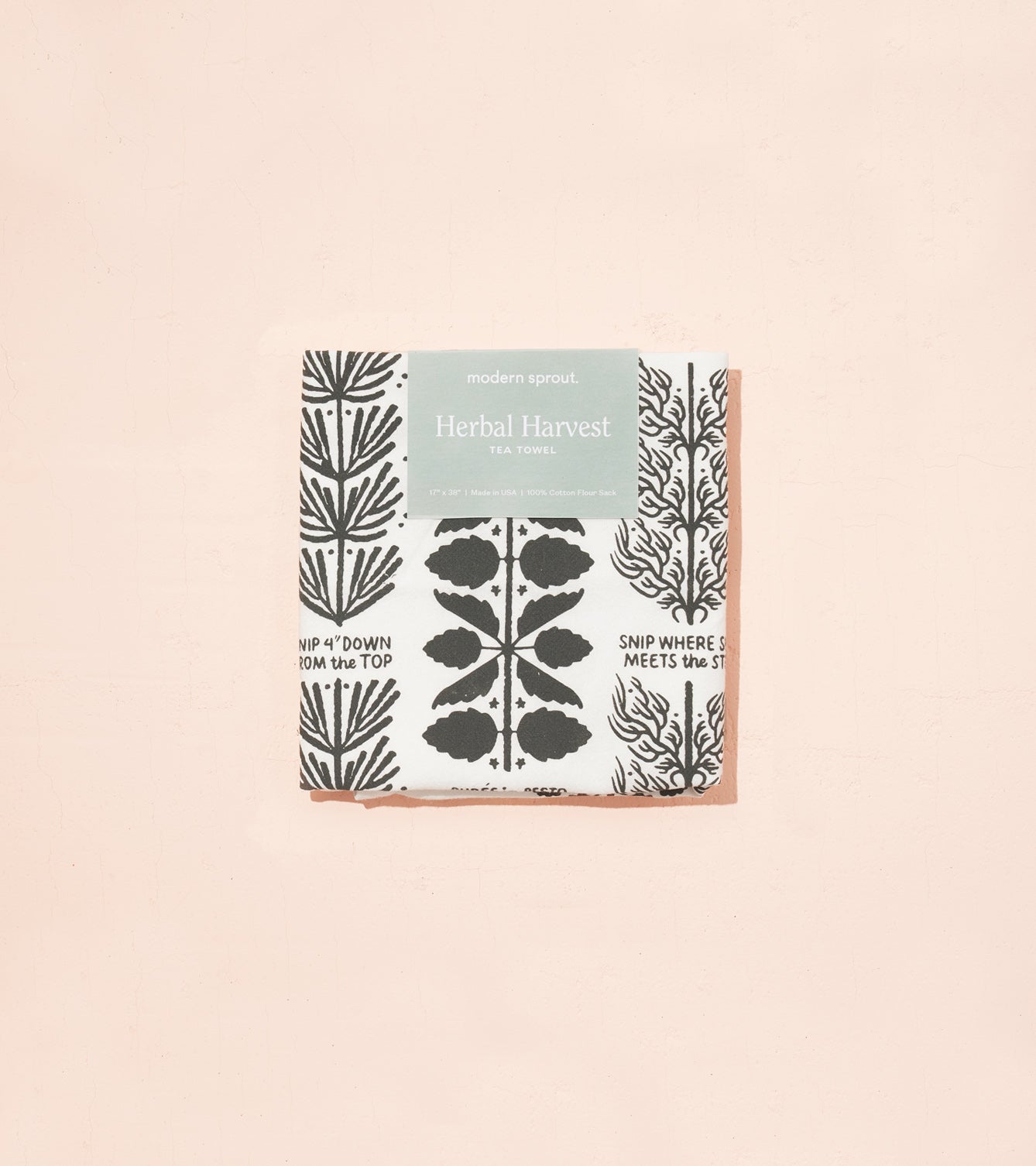 Herbal Harvest tea towel featuring botanical illustrations in black and white with a peach border, packaged attractively.