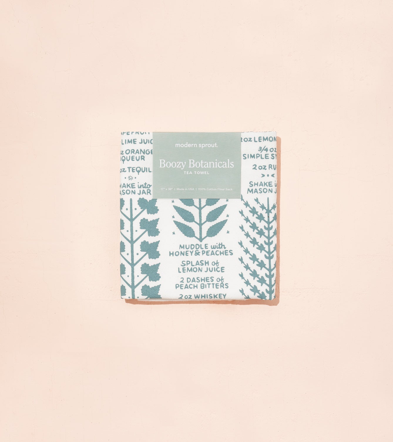 Boozy Botanicals tea towel featuring a botanical print with recipe text in blue and white, packaged neatly.