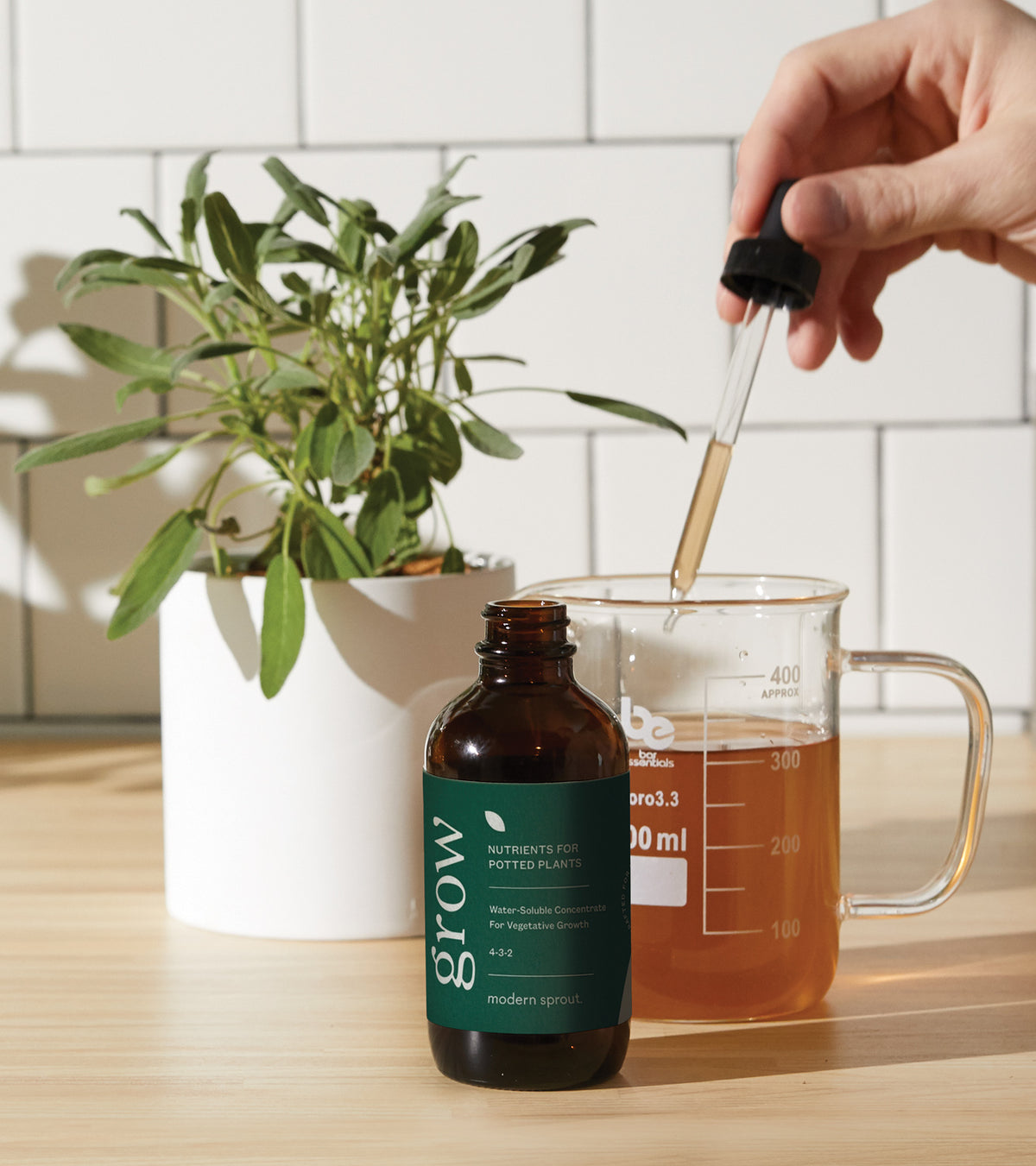 Bottle of plant nutrients with dropper, next to a potted plant and measuring cup filled with liquid.