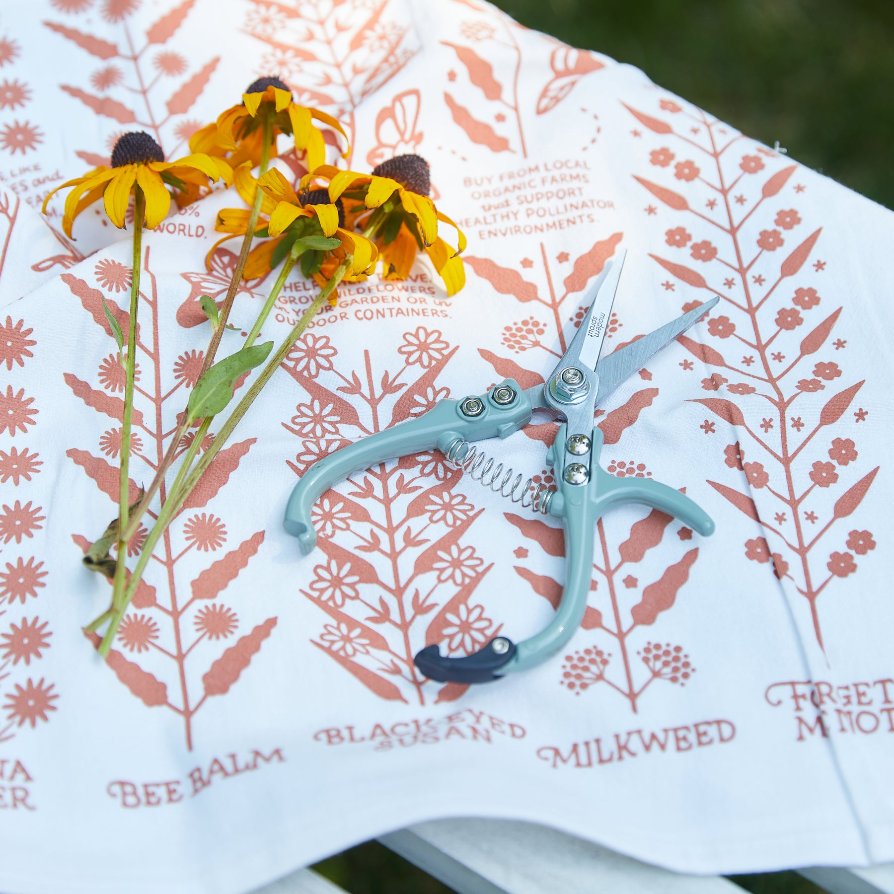 Gardening shears and pruners on a patterned cloth with yellow flowers, showcasing tools for plant care and maintenance.
