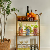 Stylish bar cart featuring garden jars with organic herbs, decorative bottles, and glasses, set against a neutral wall.