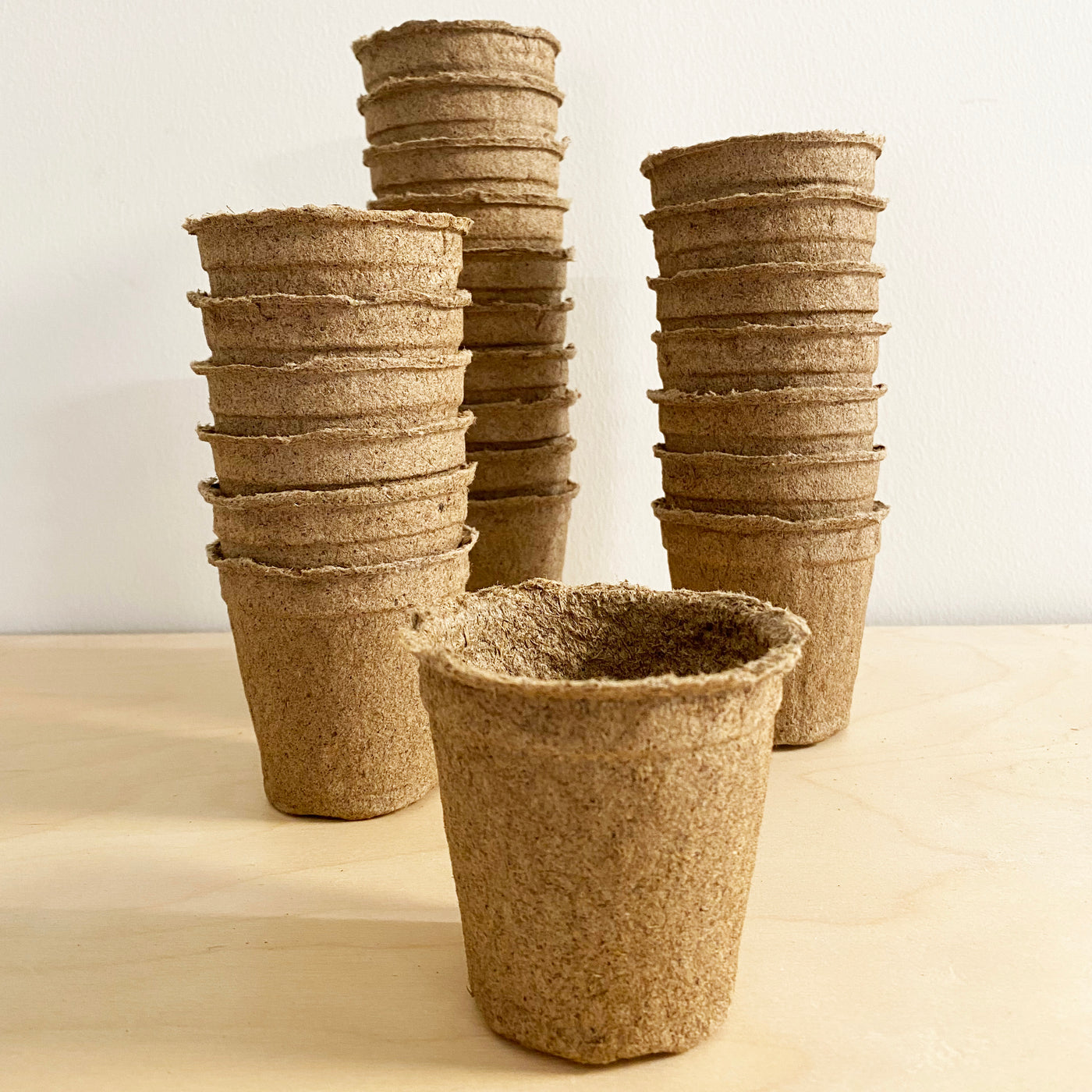 Set of 24 biodegradable 3-inch CowPots stacked and arranged on a wooden surface, ideal for planting seedlings.